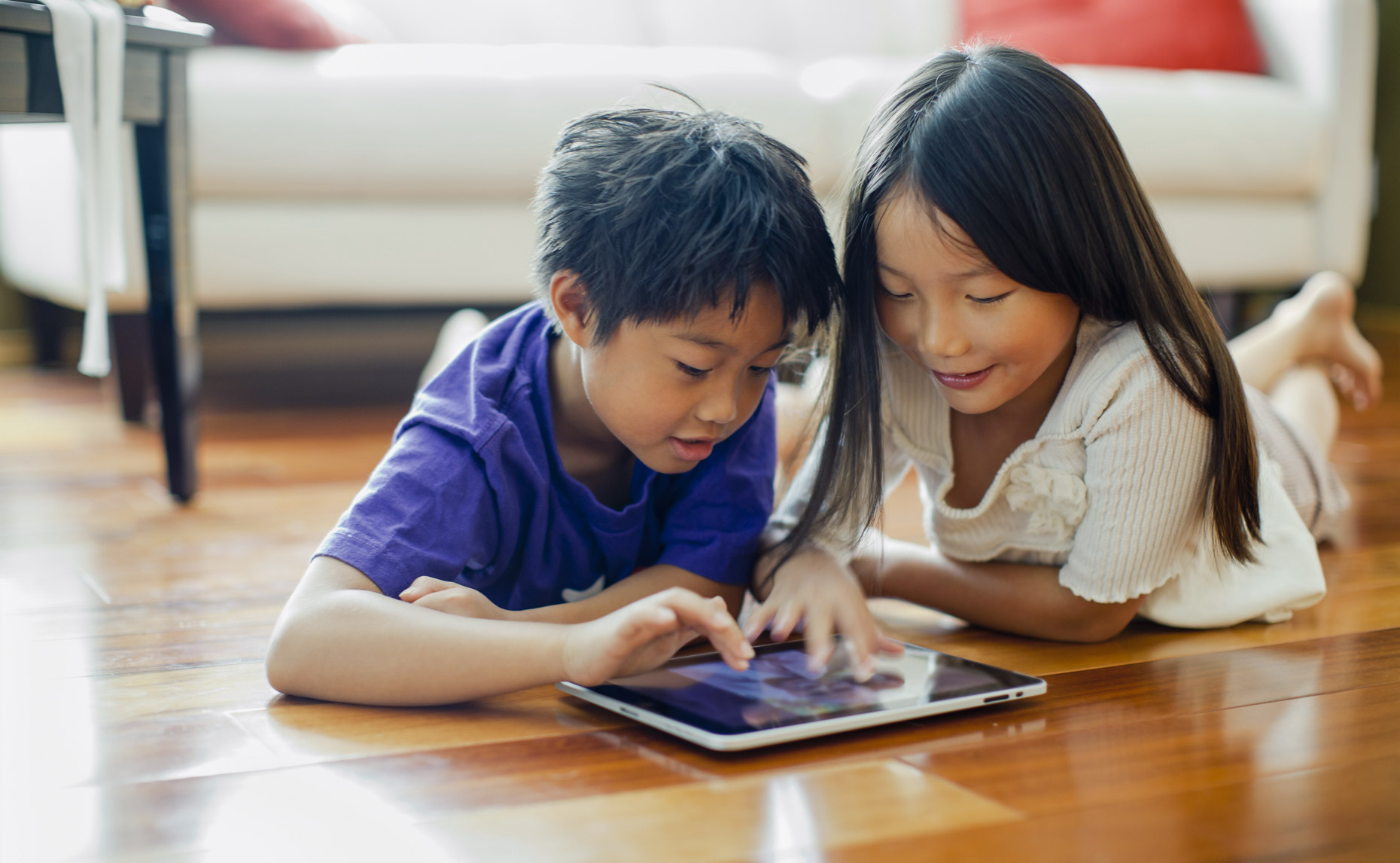 Asian boy and girl laying on floor playing on ipad
