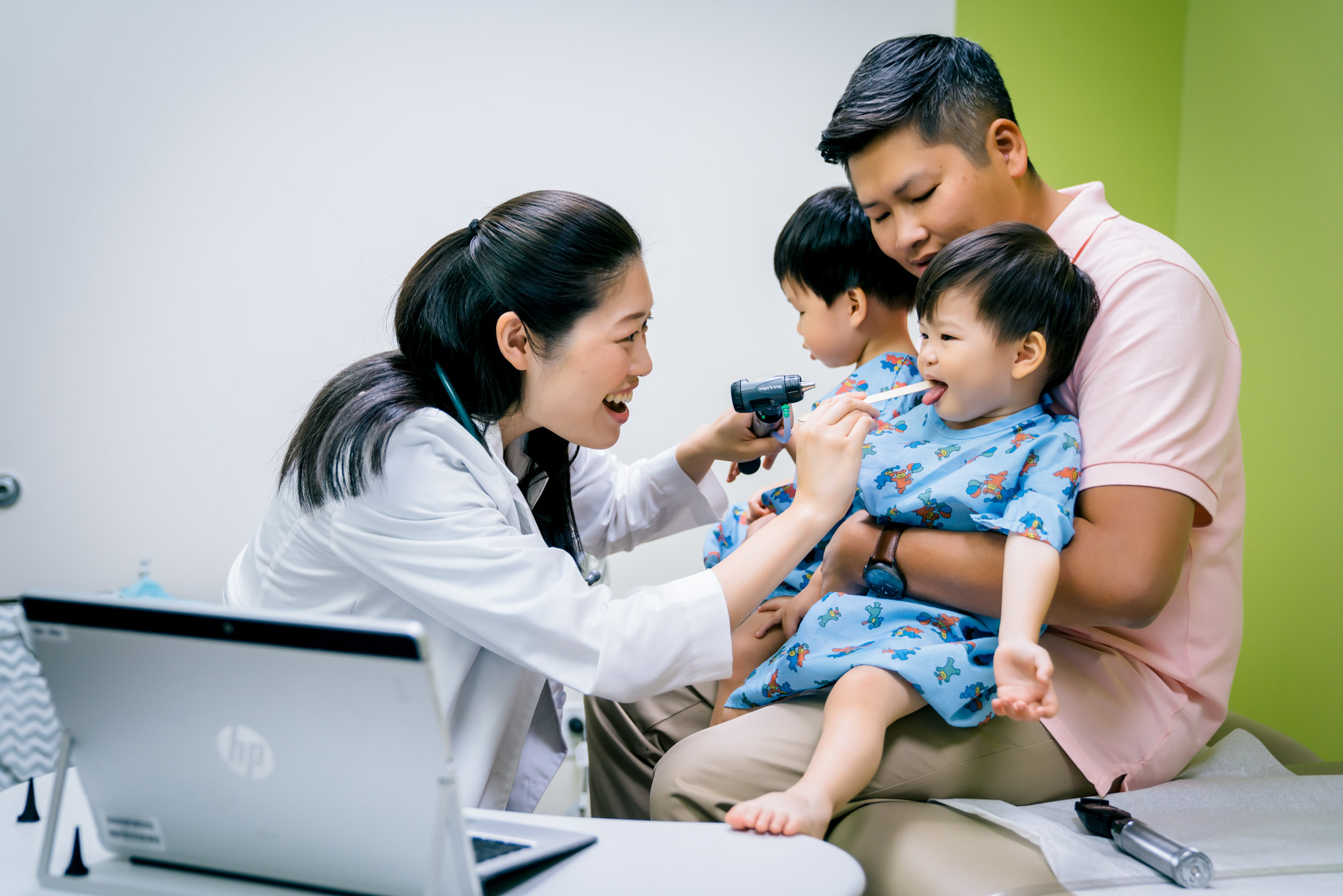 Female pediatrician examining twin boy toddlers sitting on dad