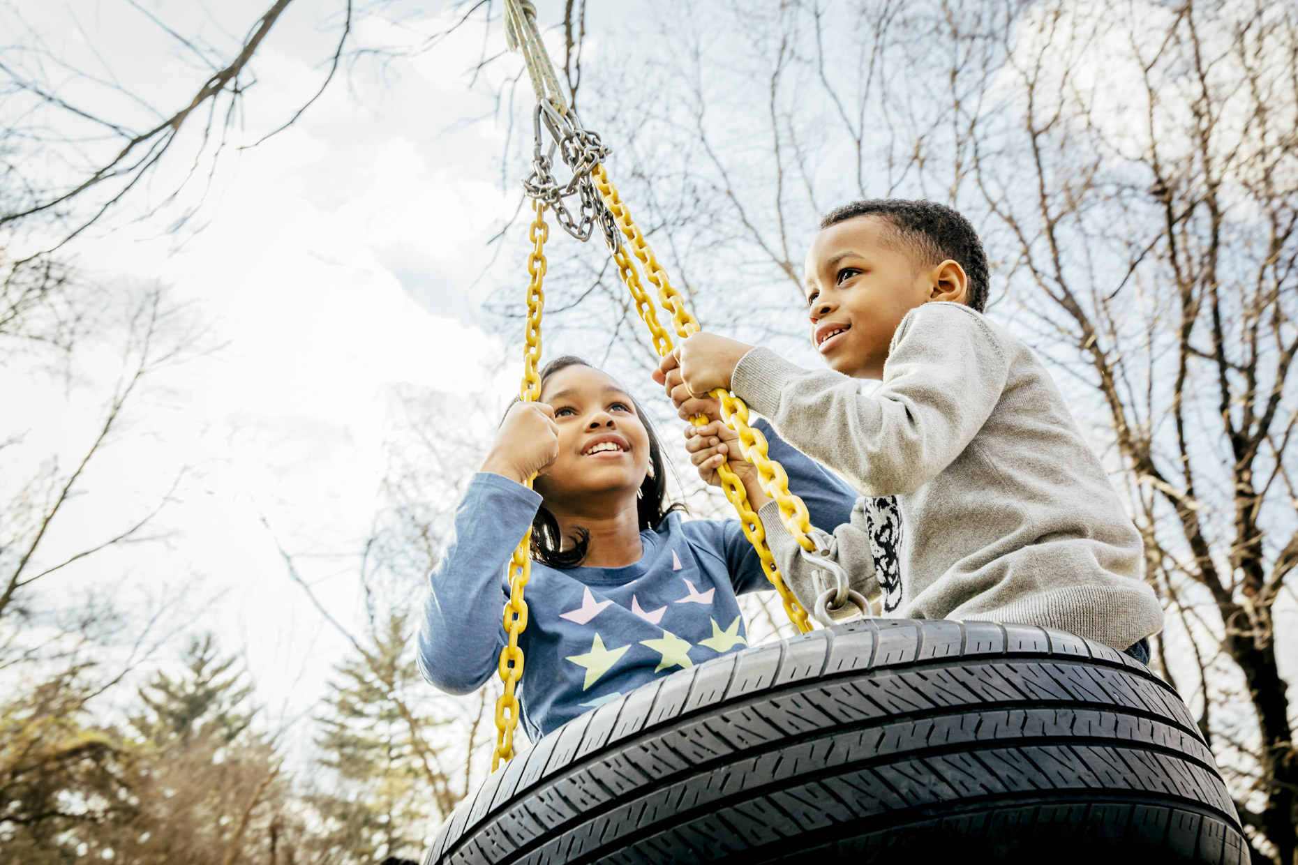 Black boy and girl swinging on tire swing in fall