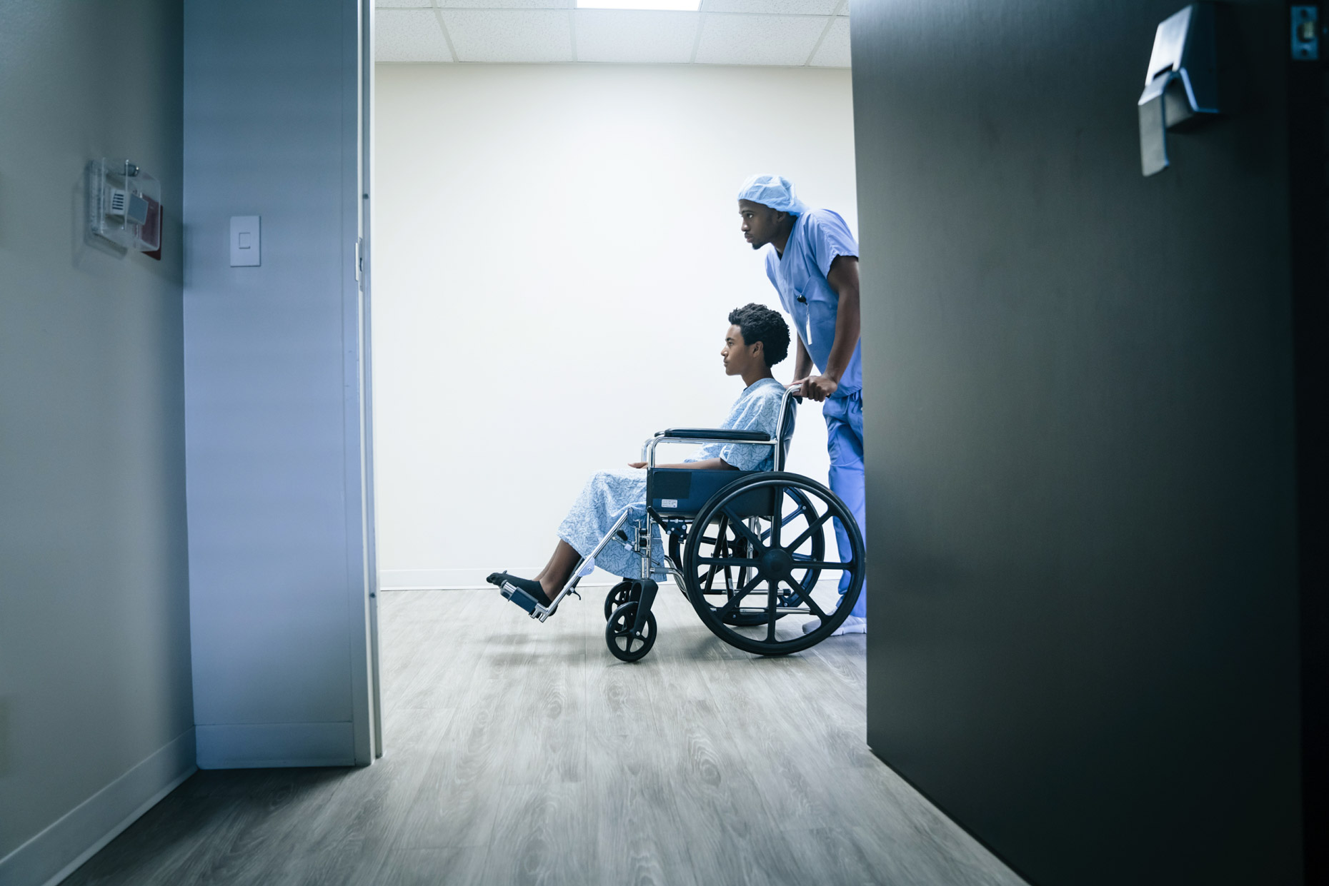 Black male nurse wheeling teen in wheel chair through hospital