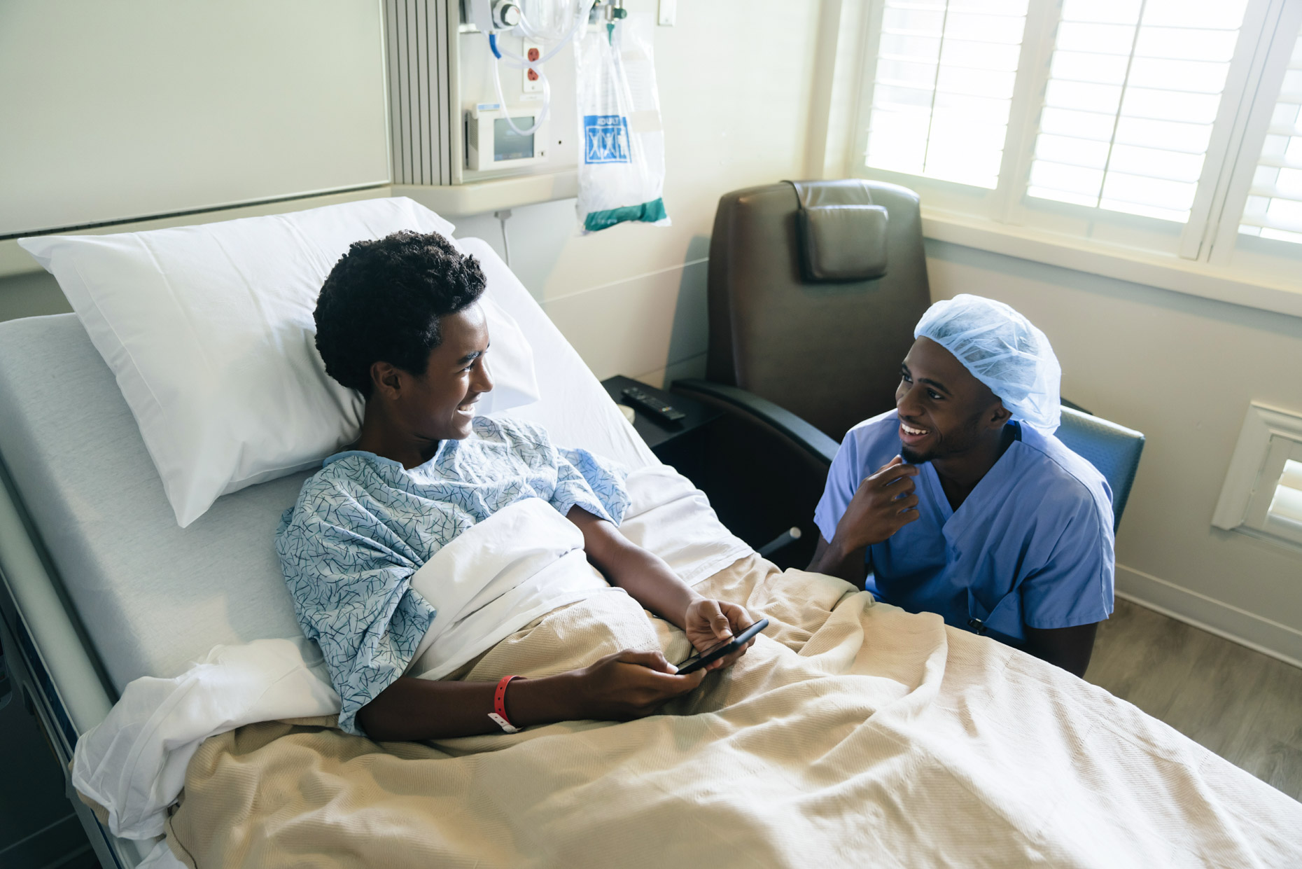 Black male nurse talking to teen patient in hospital bed