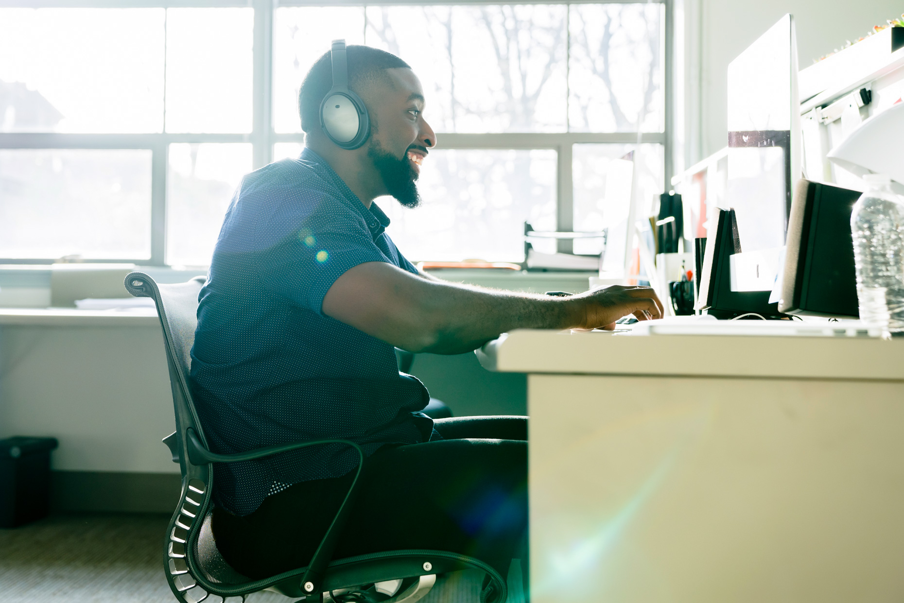 Black man with wireless headphones working in office on computer
