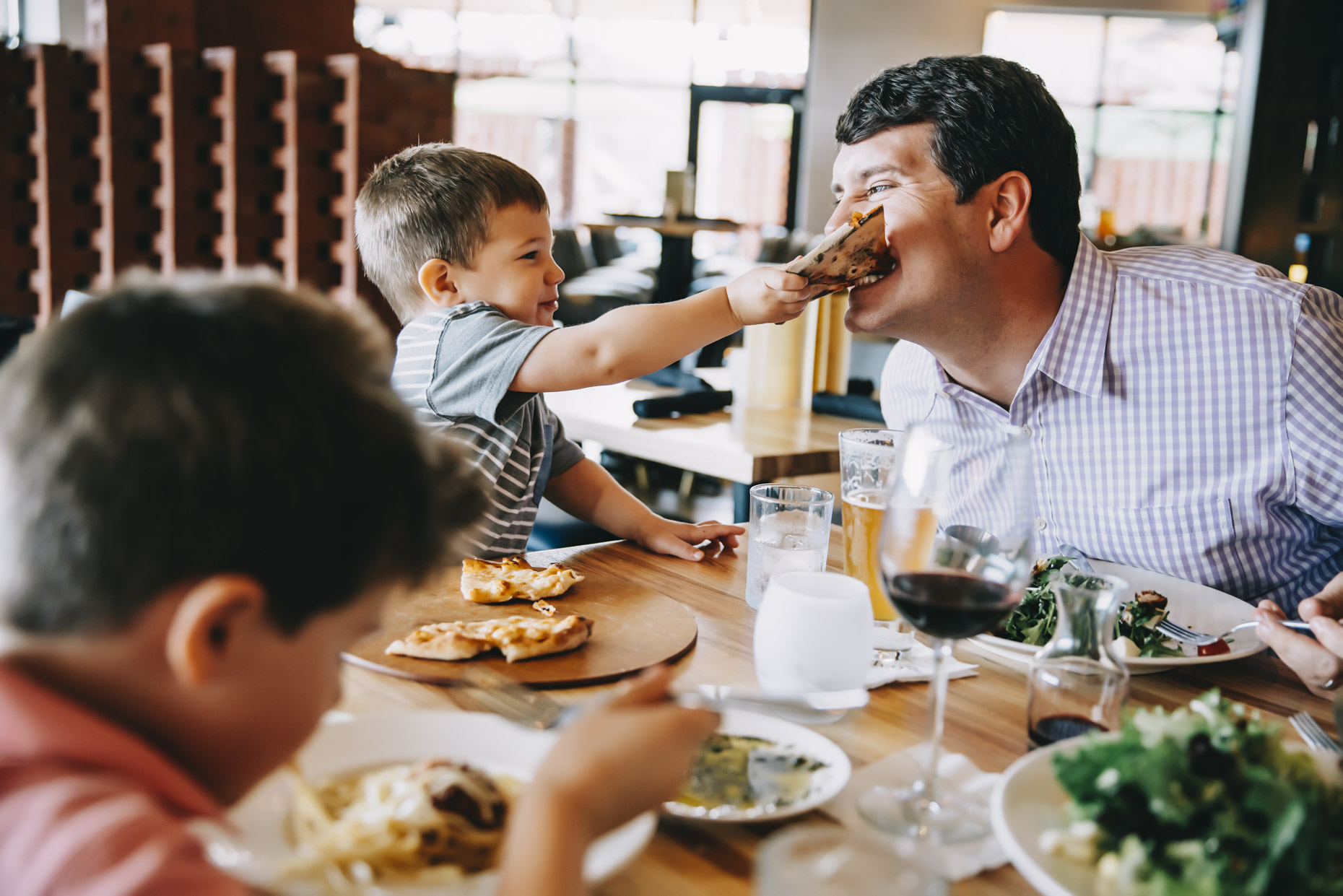 Boy feeding dad bite of his pizza in restaurant