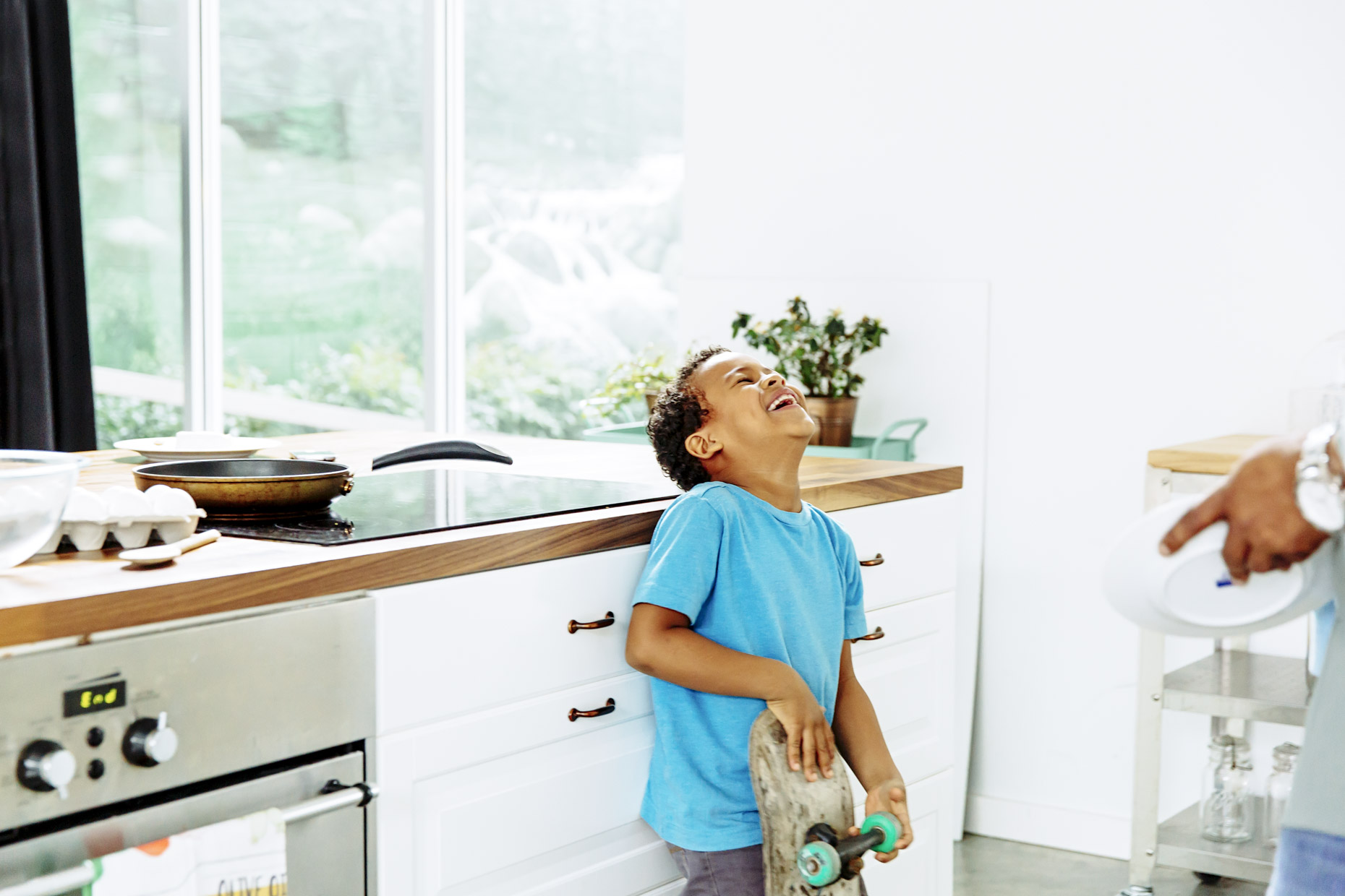 Boy holding skateboard in kitchen with head back laughing