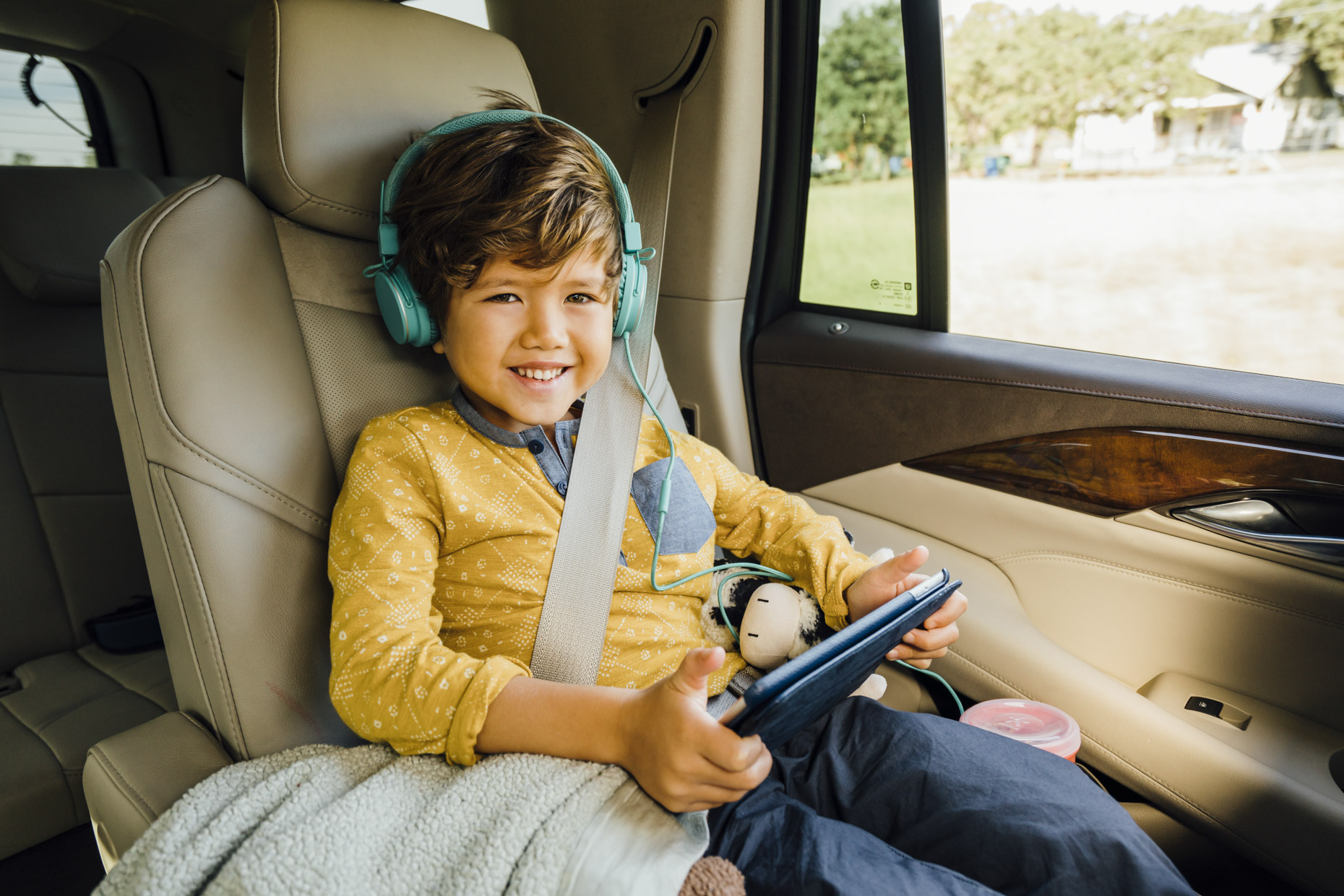 Smiling boy in car with headphones and ipad tablet computer