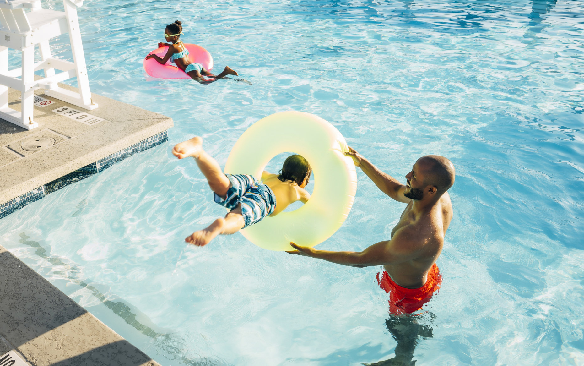 Boy jumping through pool doughnut held by dad at hotel resort pool