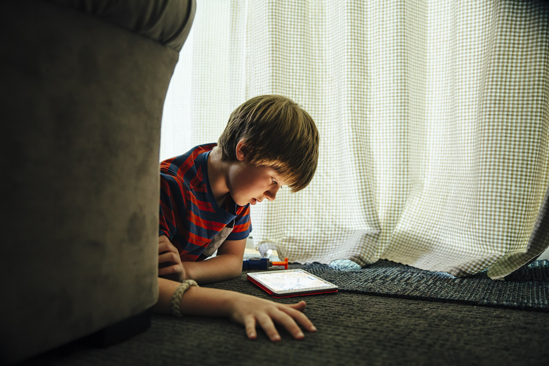 Boy laying on floor by couch reading in ipad computer tablet