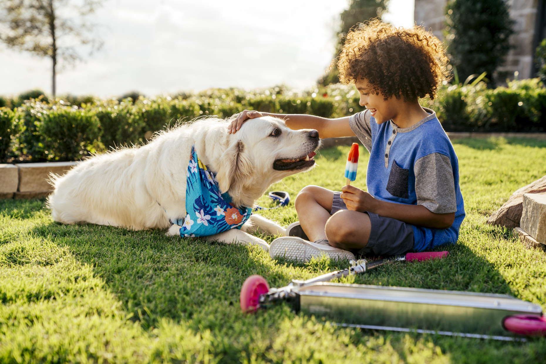 Boy sitting in yard petting dog and eating popsicle