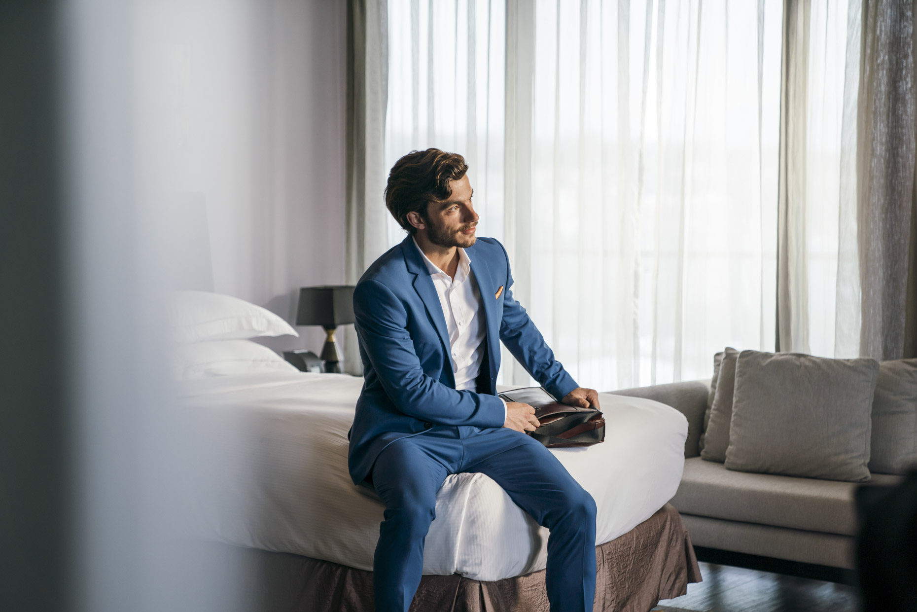 Business man sitting on bed in Hilton hotel with briefcase
