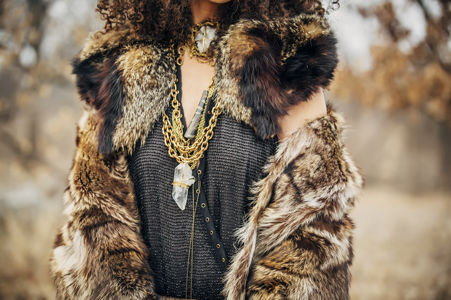 Close up woman in long dress and fur coat with brass and white crystal Belthazzar Jewels necklaces outside in fall