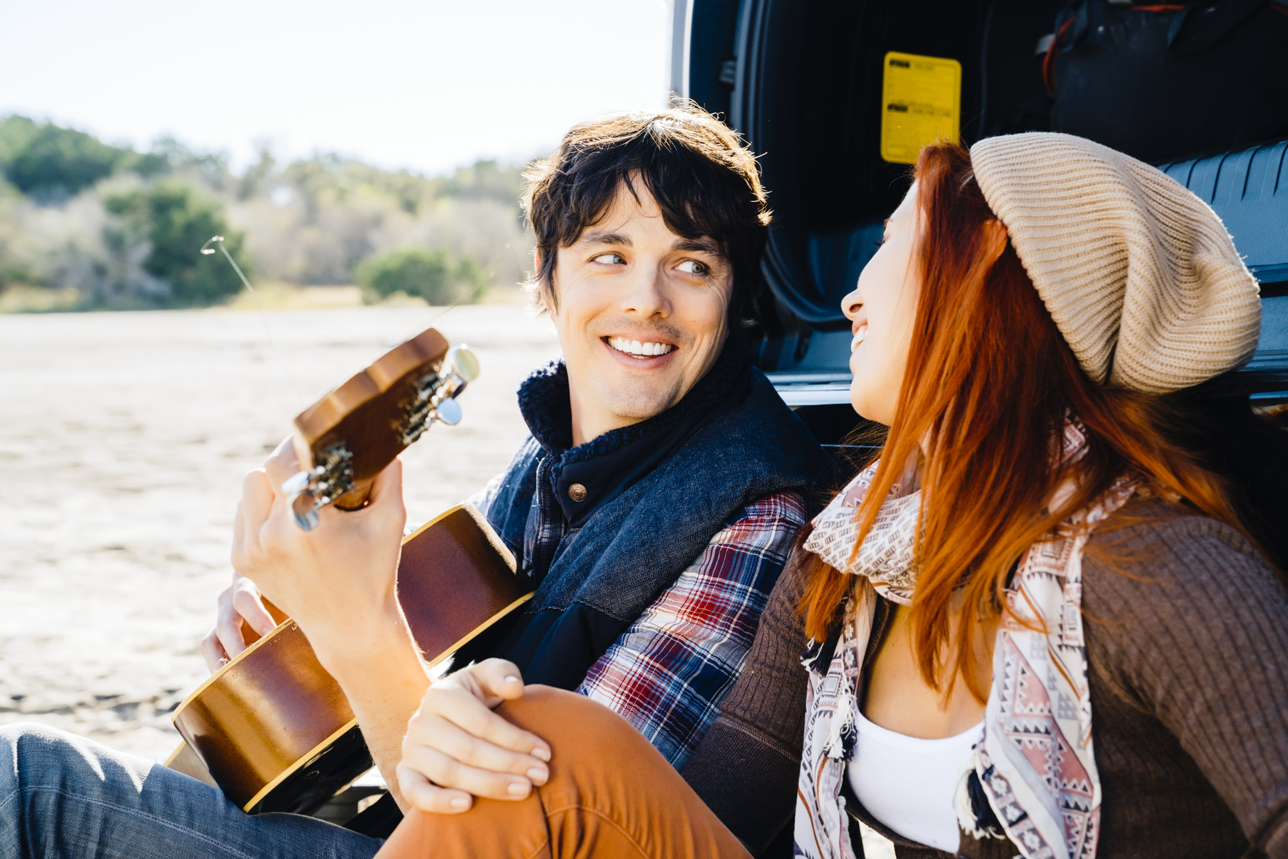 Couple sitting by truck playing guitar