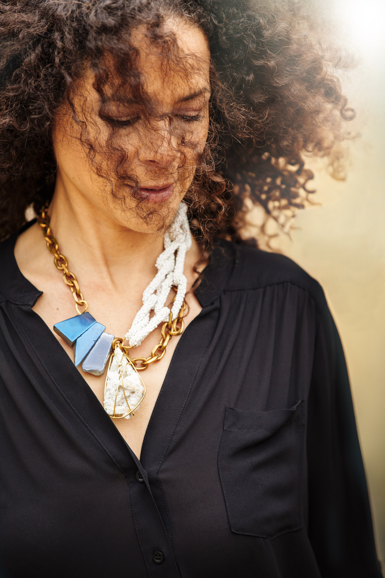 Curly haired woman in all black with Belthazzar Jewels brass and stone necklace