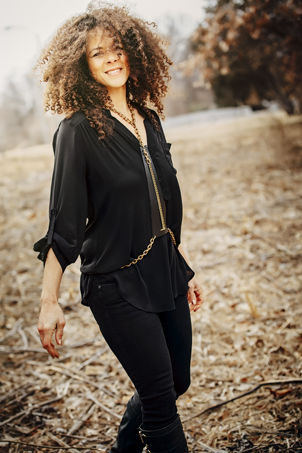 Curly haired woman in all black with Belthazzar Jewels brass and leather harness