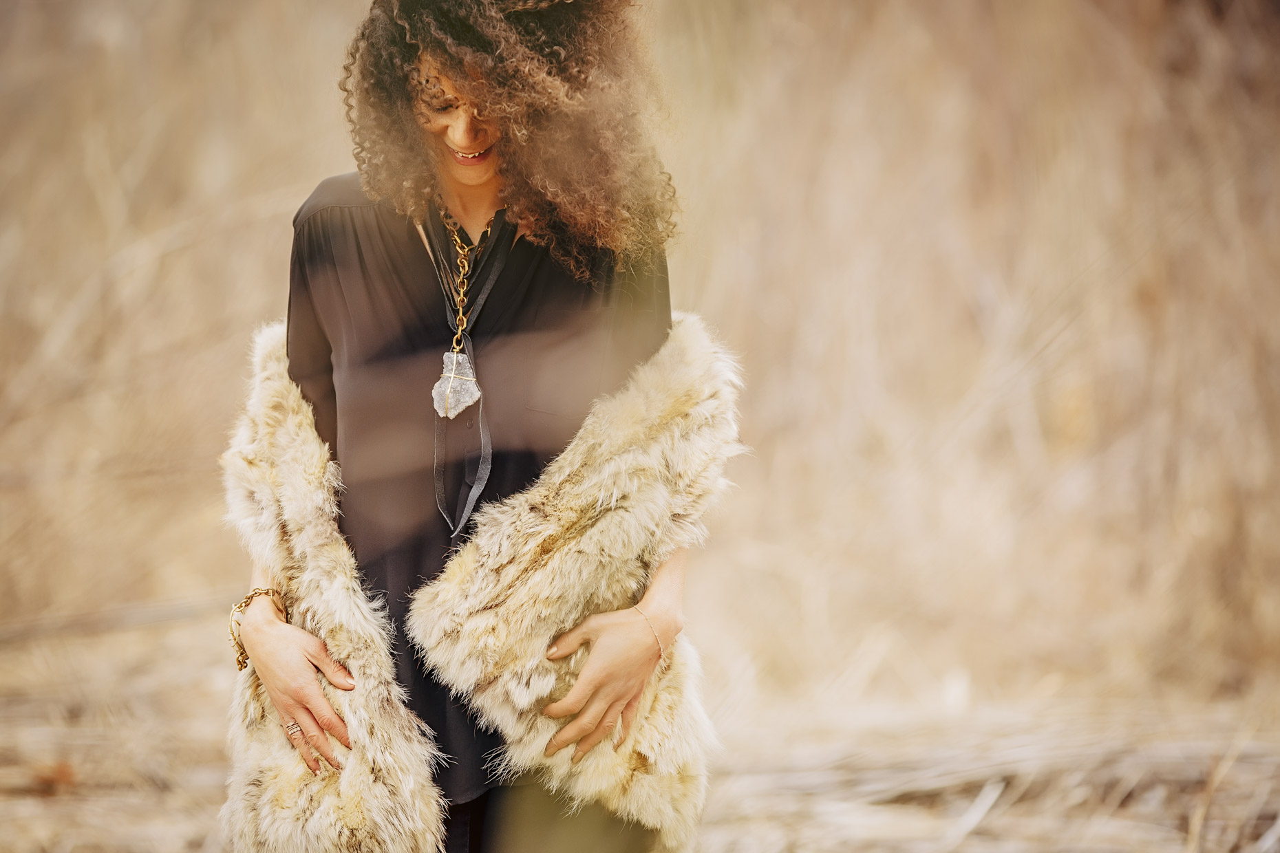 Curly haired woman in black with fur coat wearing Belthazzar Jewels brass stone necklace