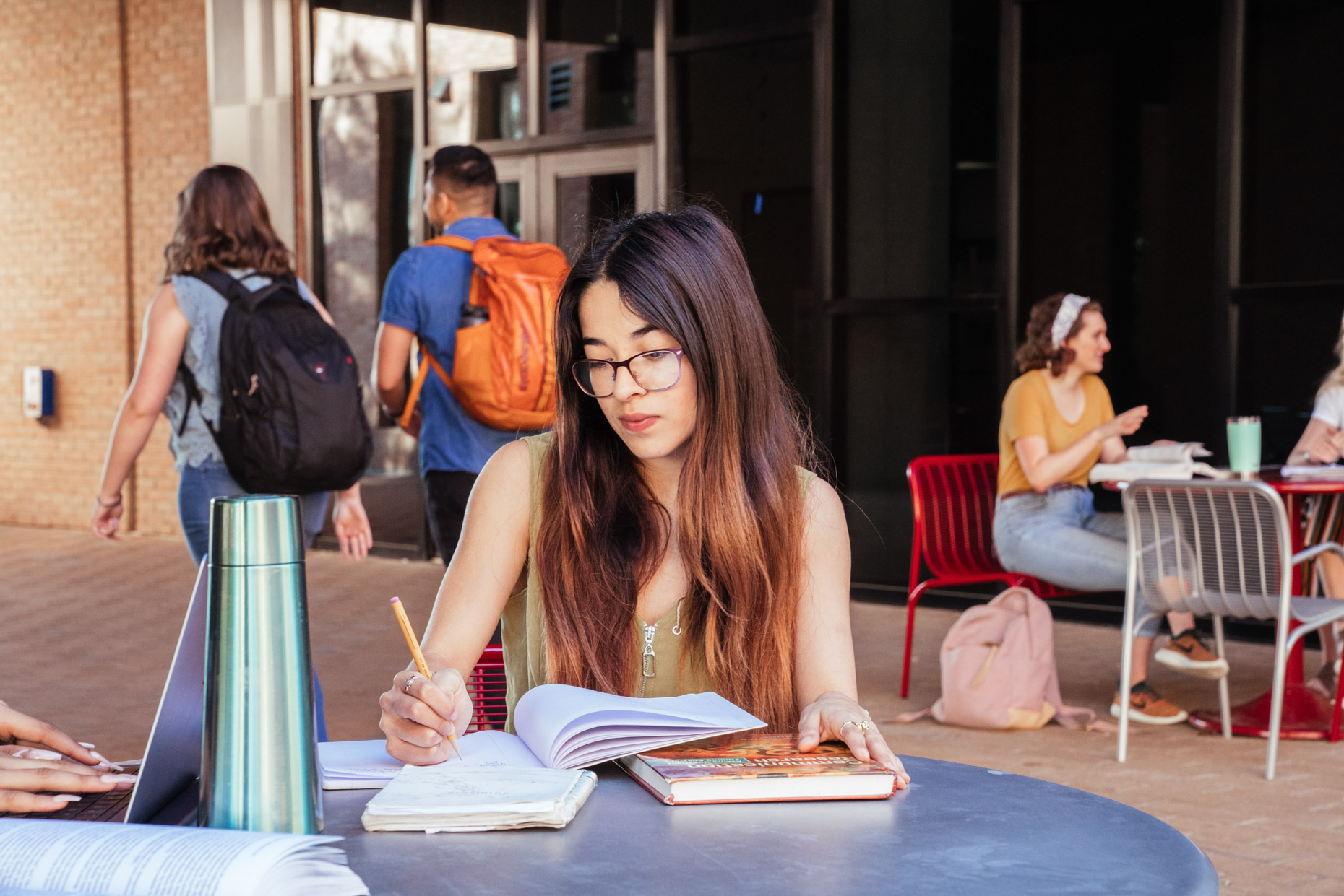 Female college student taking notes sitting at table in campus courtyard