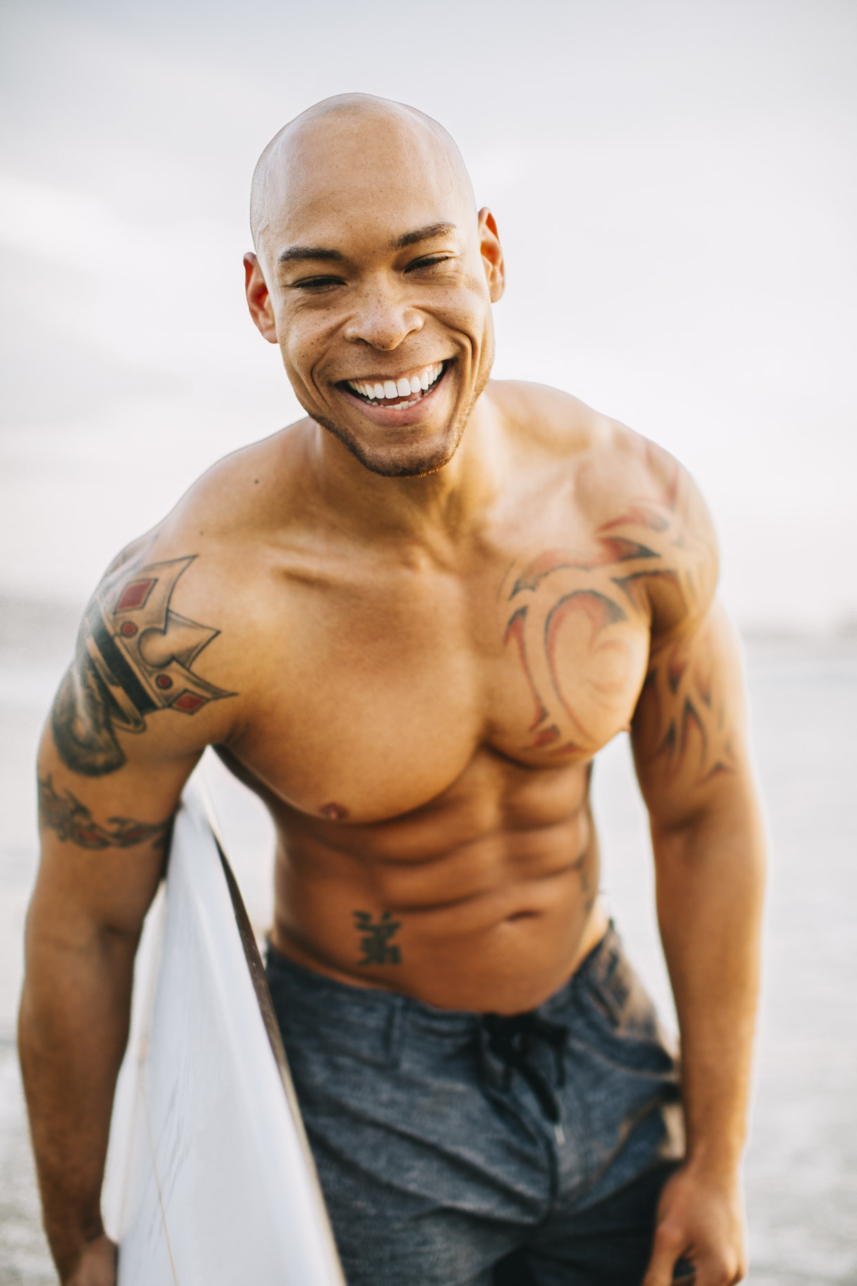 Fit man with bald head and surfboard laughing
