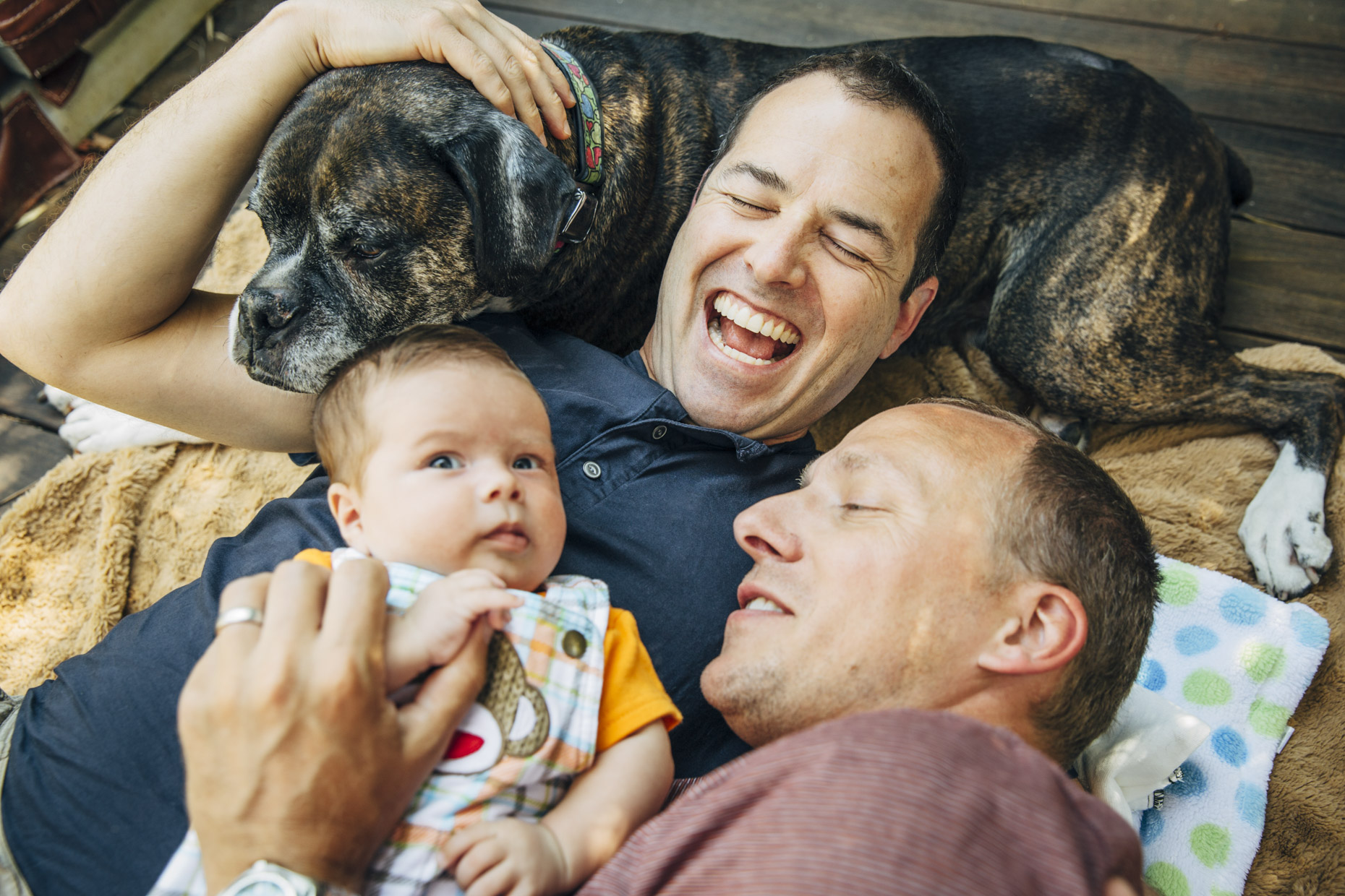 Gay dads laying down snuggling dog and baby