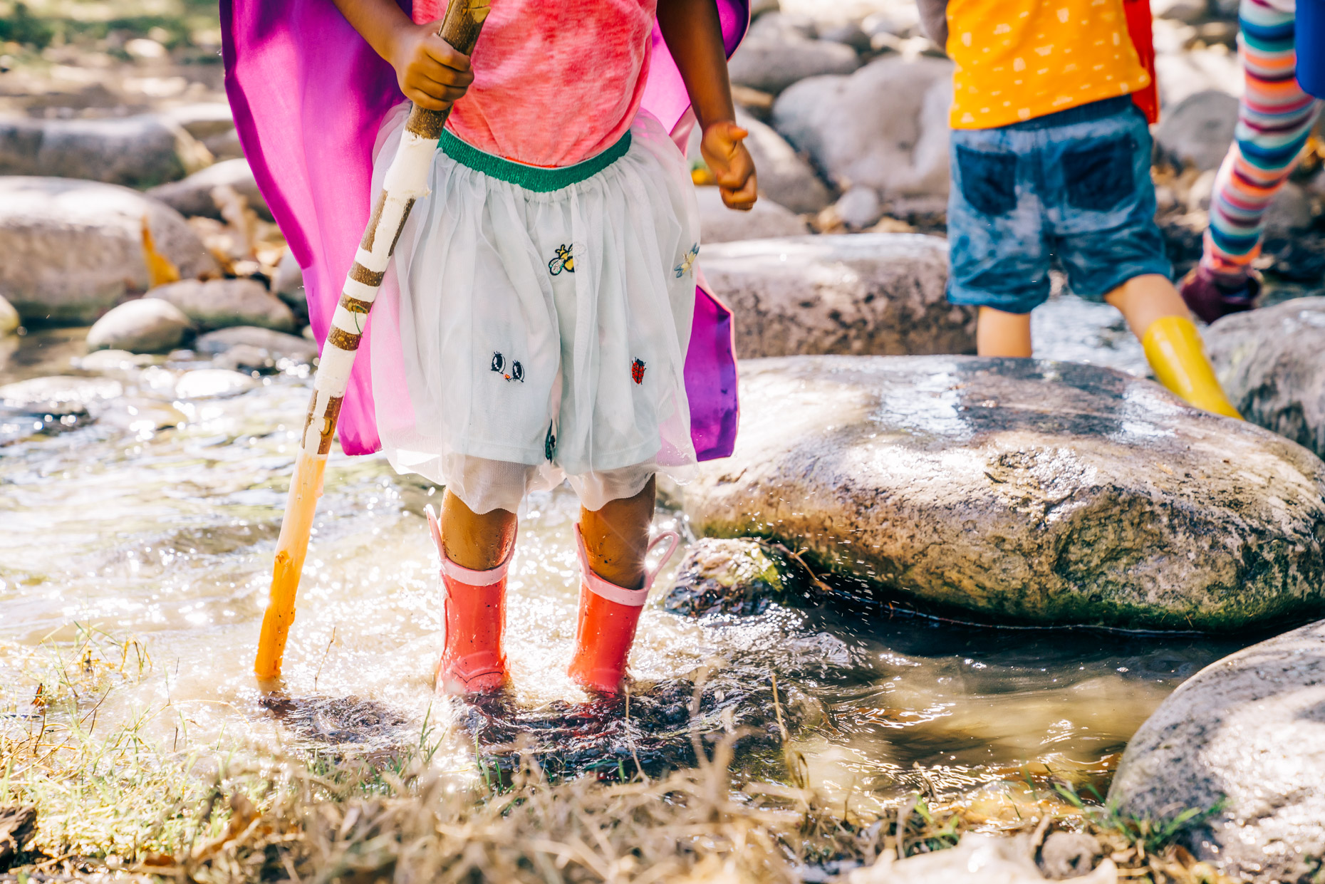 Girl in dress and rubber boots playing in creek