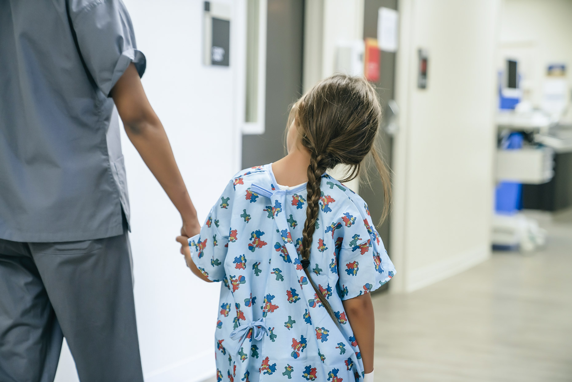 Girl hospital gown holding hands with nurse walking down halfway