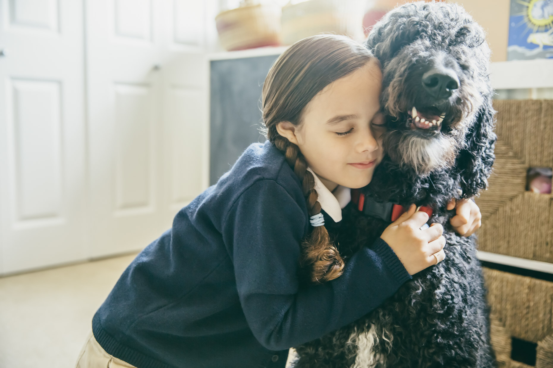 Girl in school uniform hugging labradoodle dog