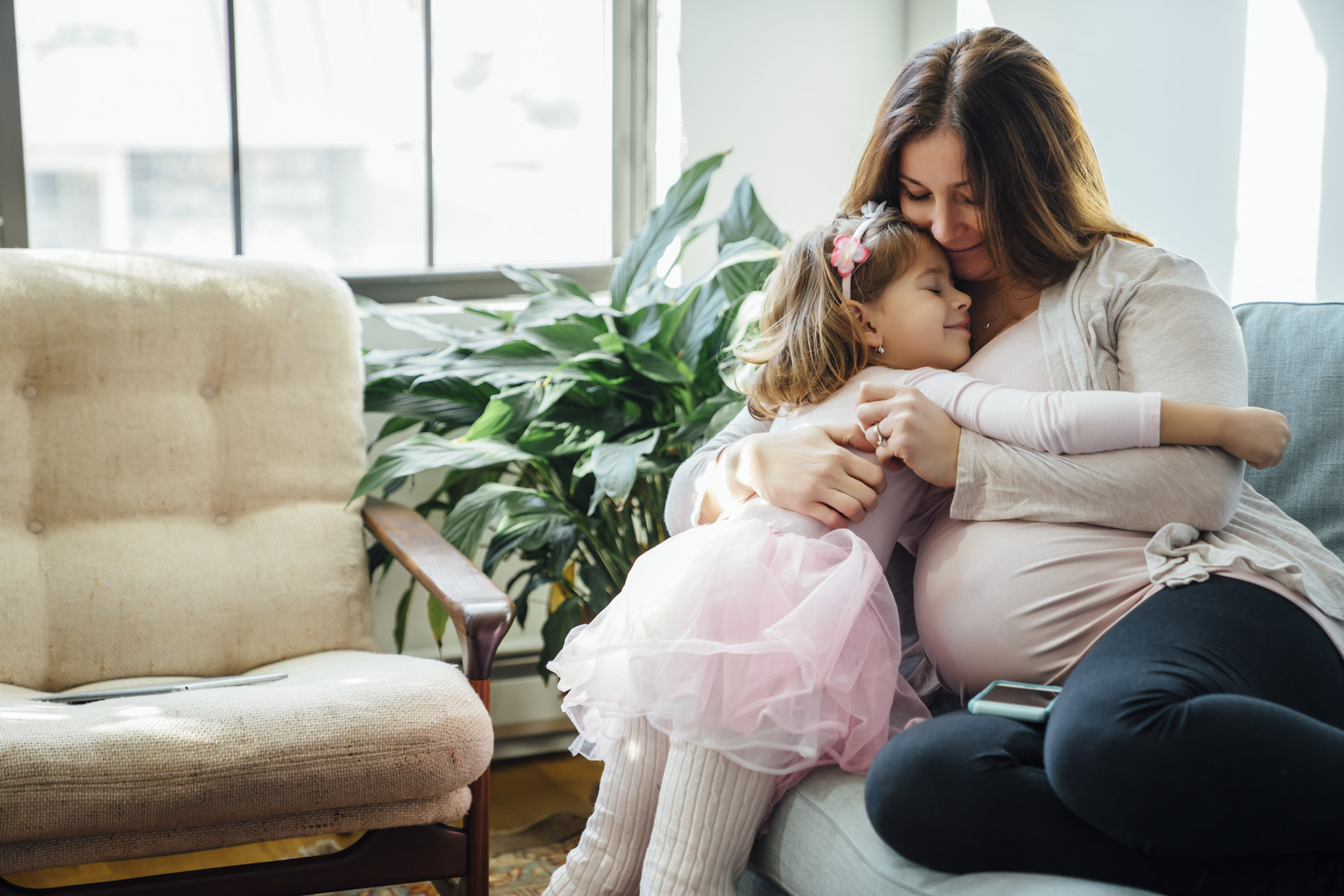 Girl in tutu hugging pregnant mom on couch