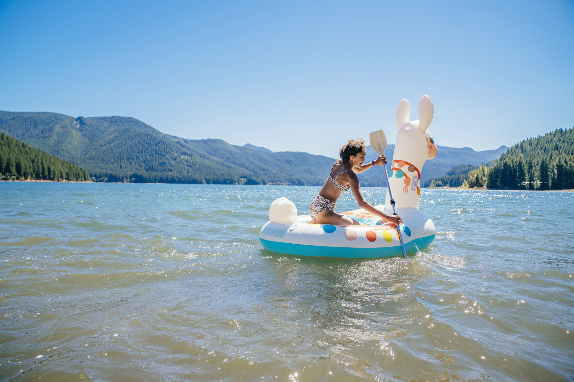 Girl paddling llama float on lake in forest