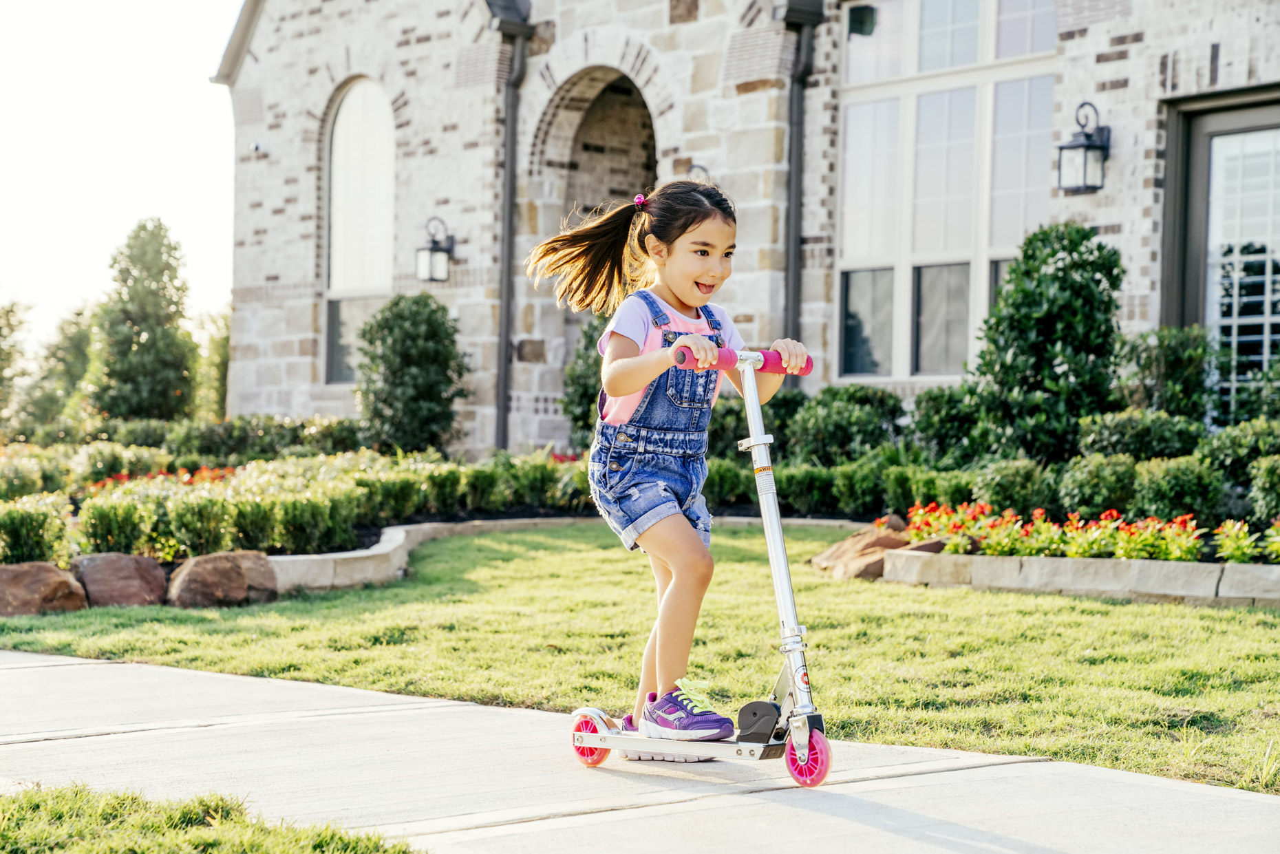 Girl riding scooter on sidewalk in front of house