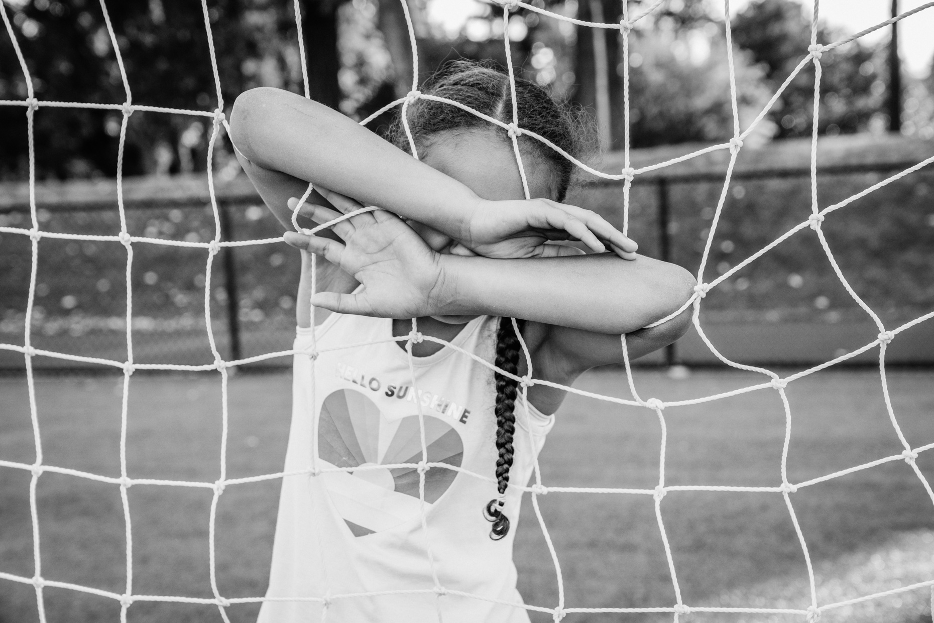 Girl with arms through soccer net covering up her face