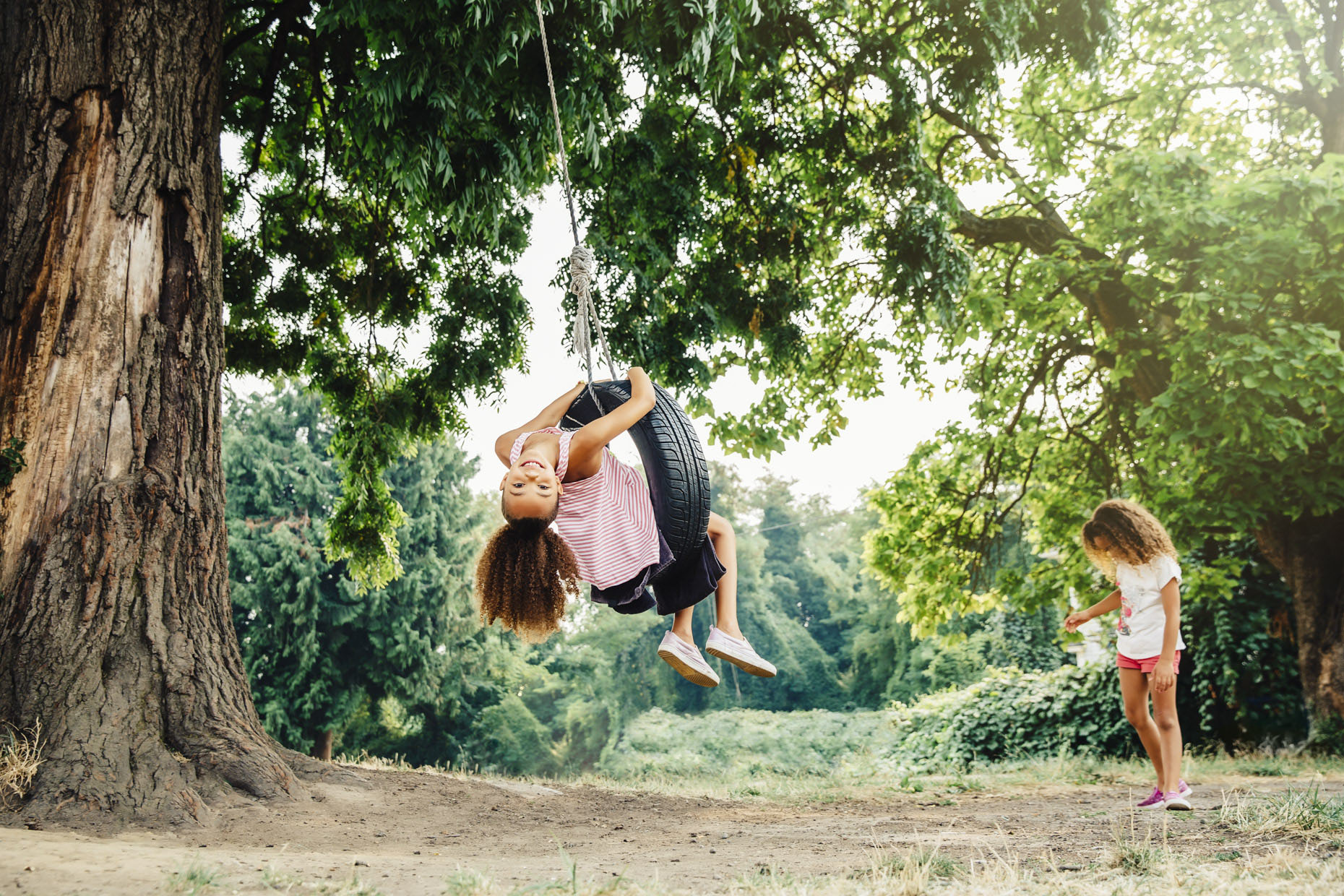 Girls playing on tire swing outside by big tree