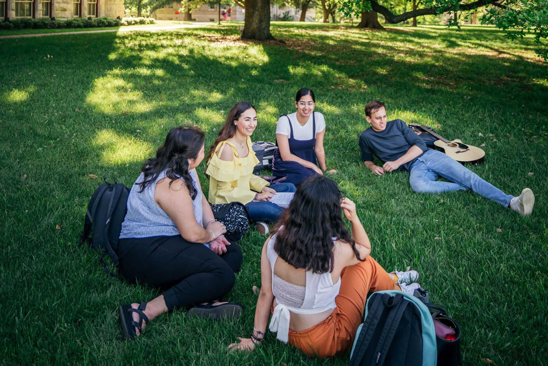 Group of happy college students hanging out on campus lawn