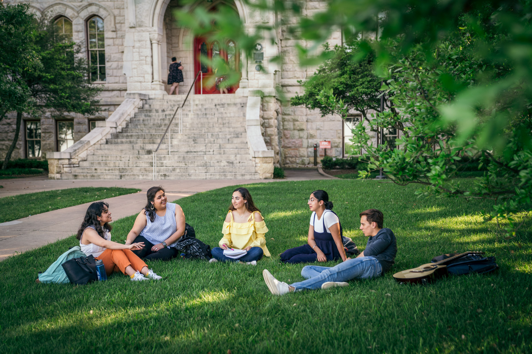 Group of happy college students hanging out on campus lawn talking