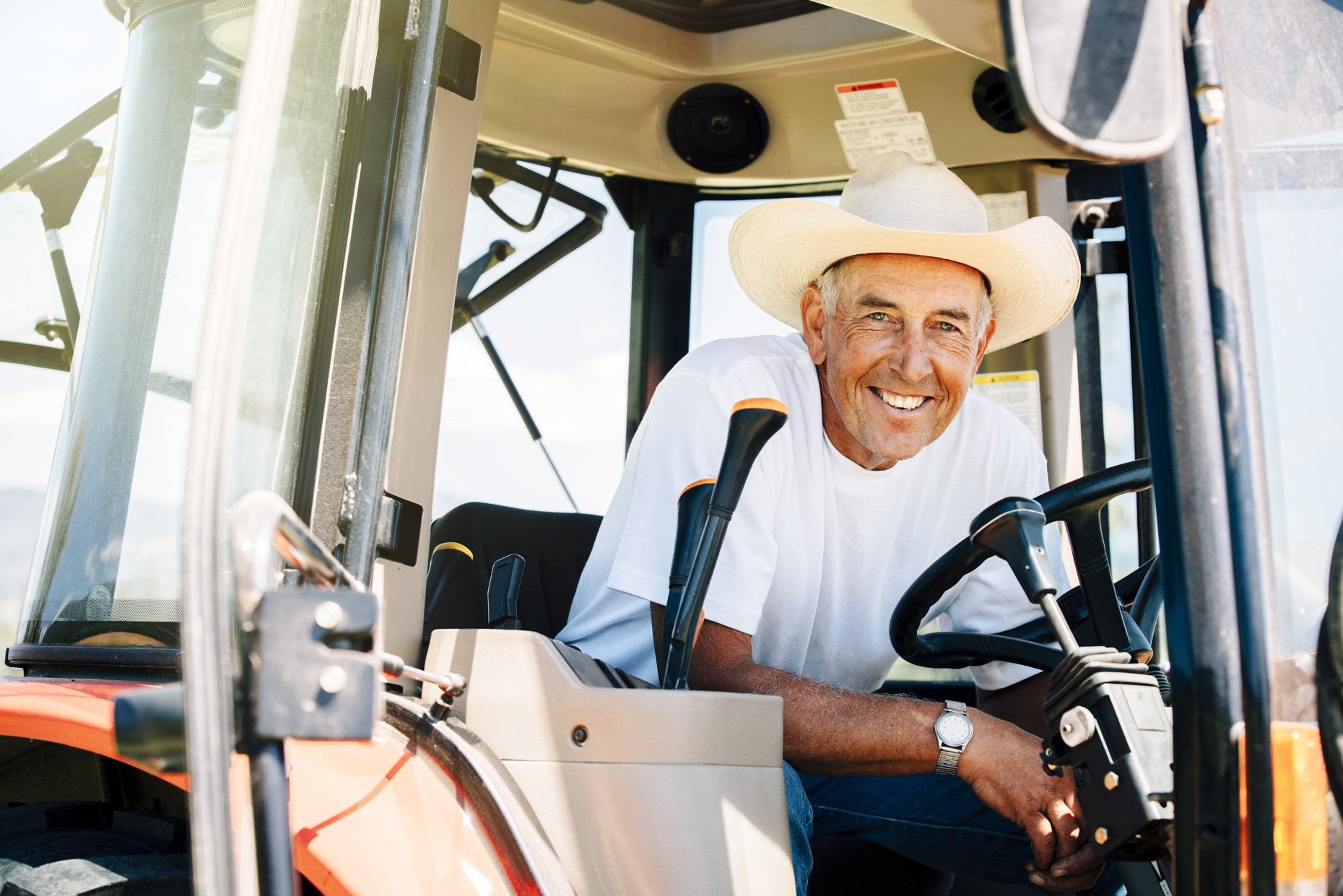 Handsome smiling senior cowboy in cab of tractor