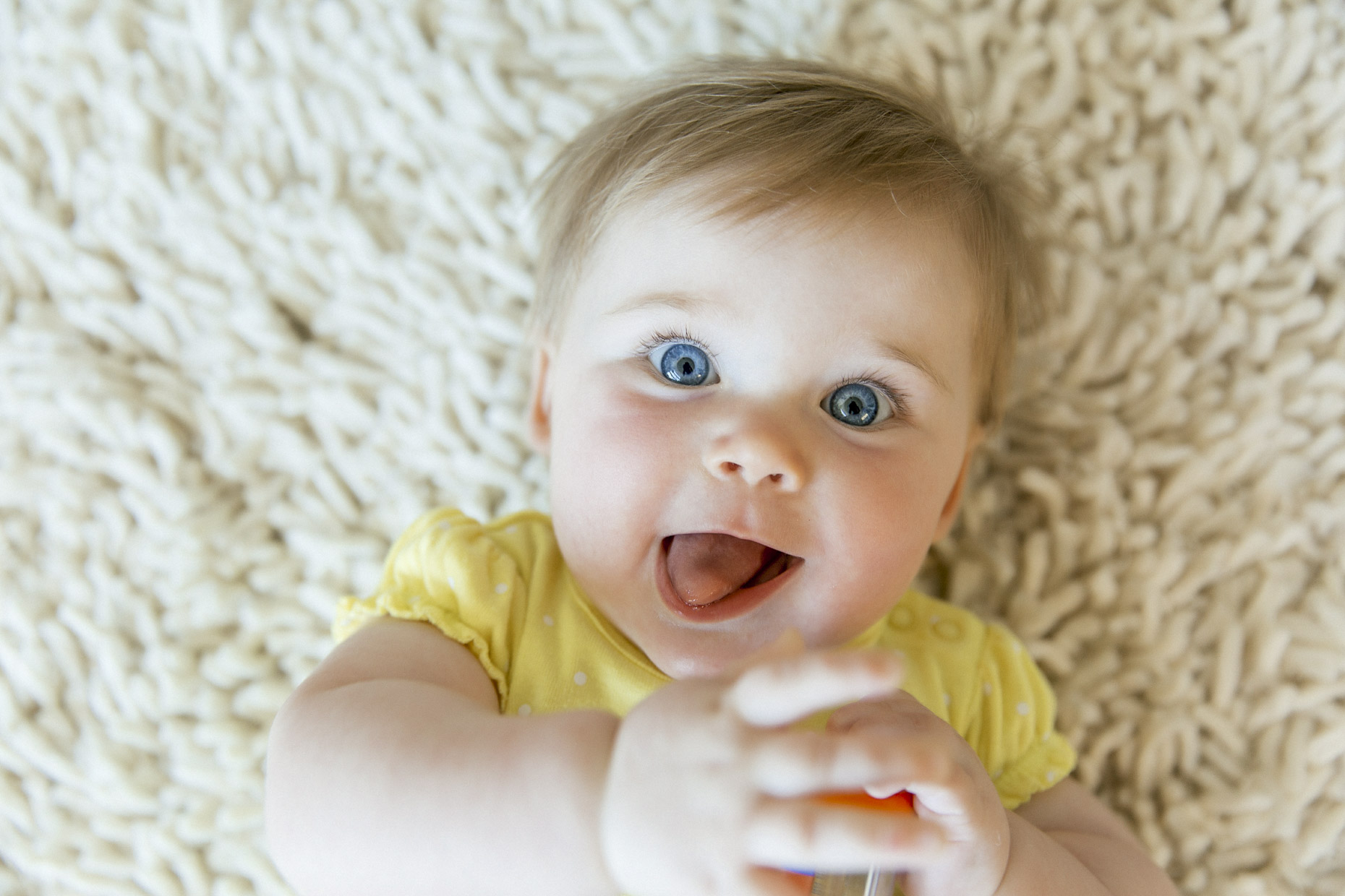 Happy baby with bright blue eyes laying on white rug