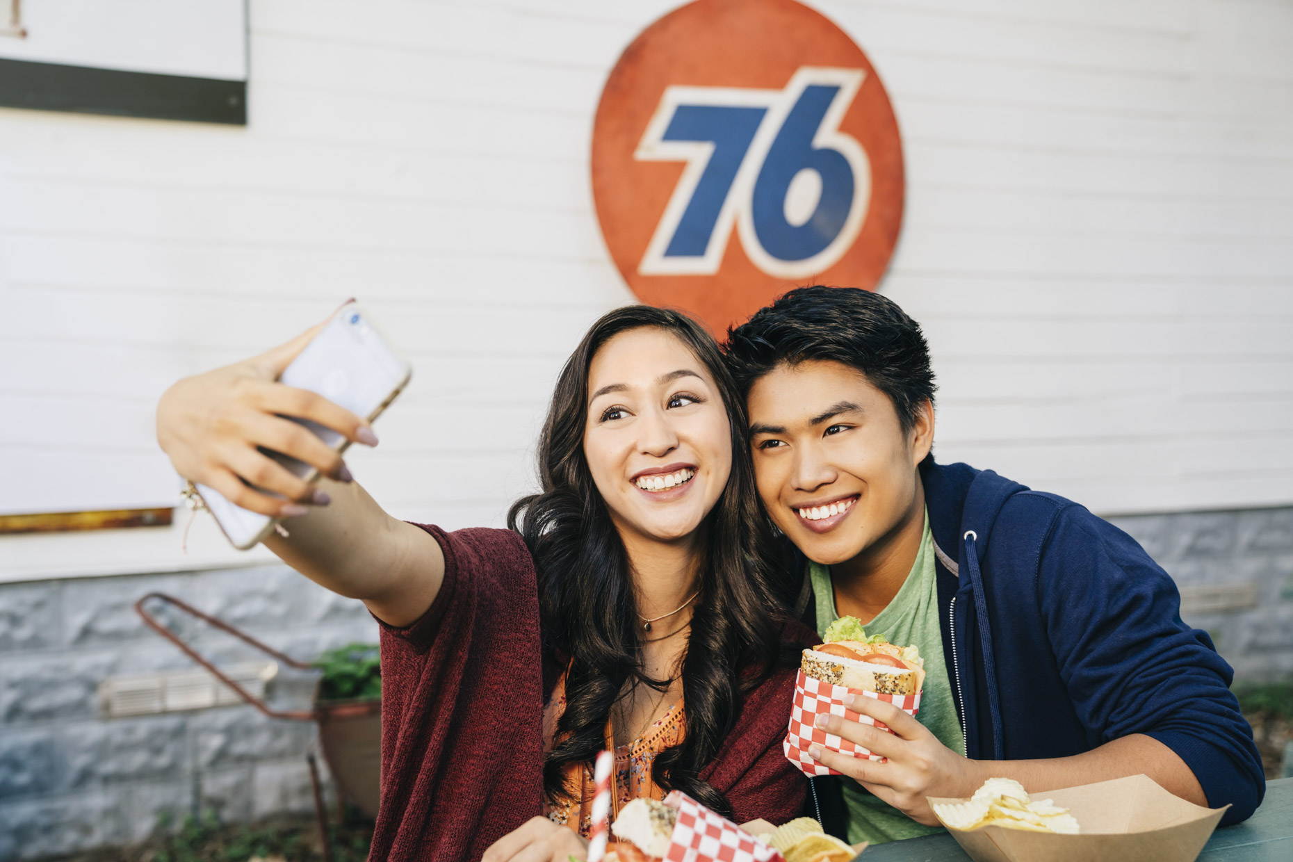Happy couple eating at outside cafe taking selfie with cell phone