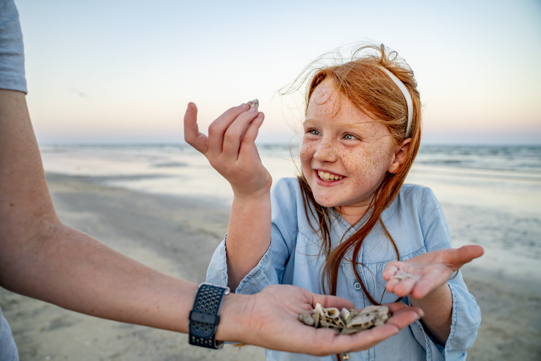 Happy girl looking at sea shells from mom