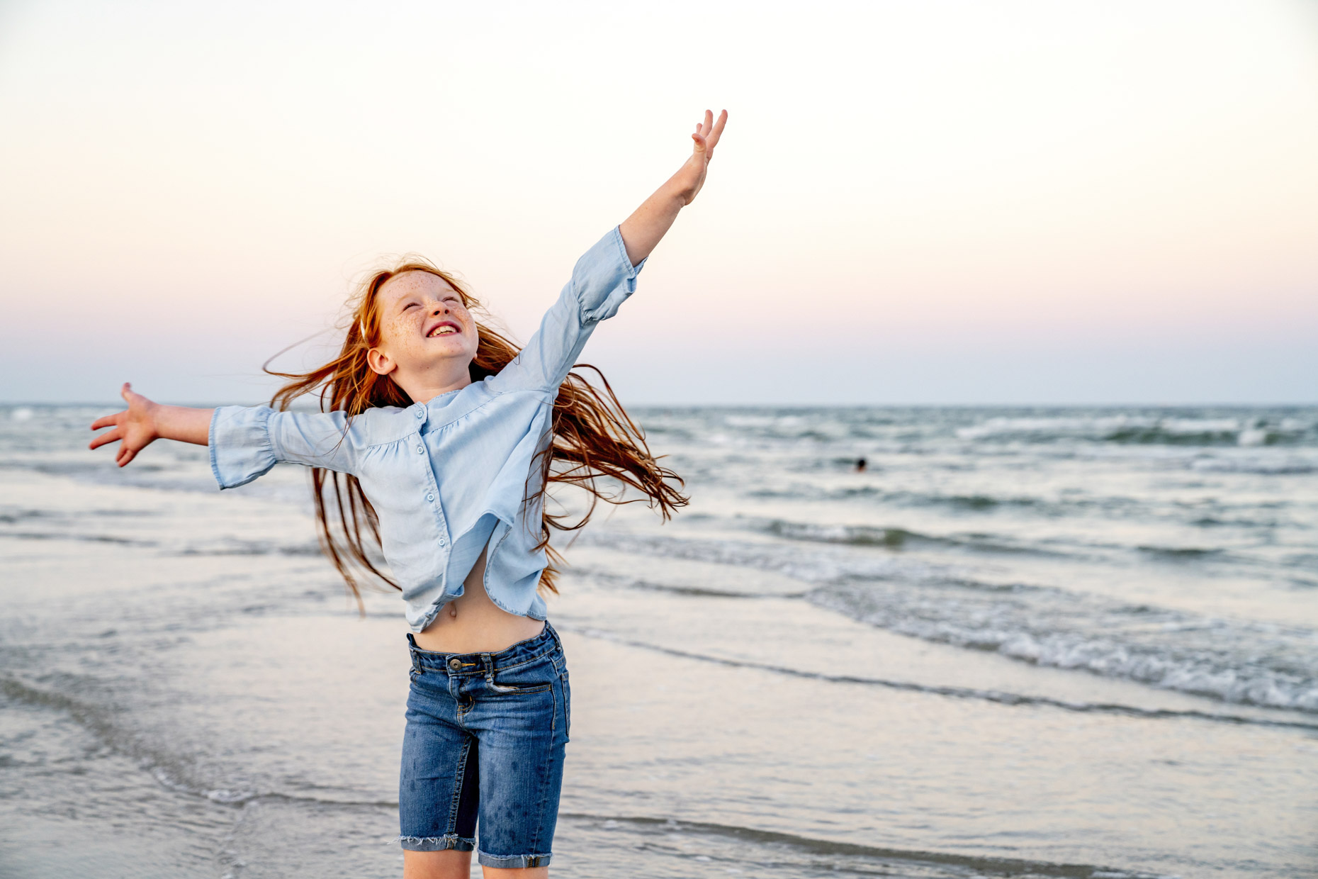 Happy red haired girl dancing on beach with arms up in air