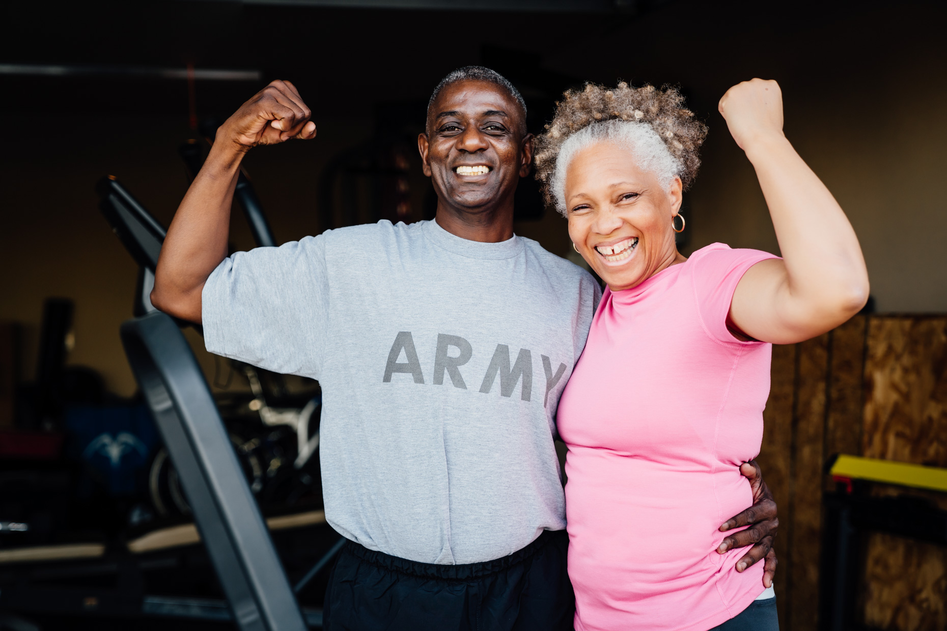 Happy senior vet couple flexing muscles in front of garage gym 