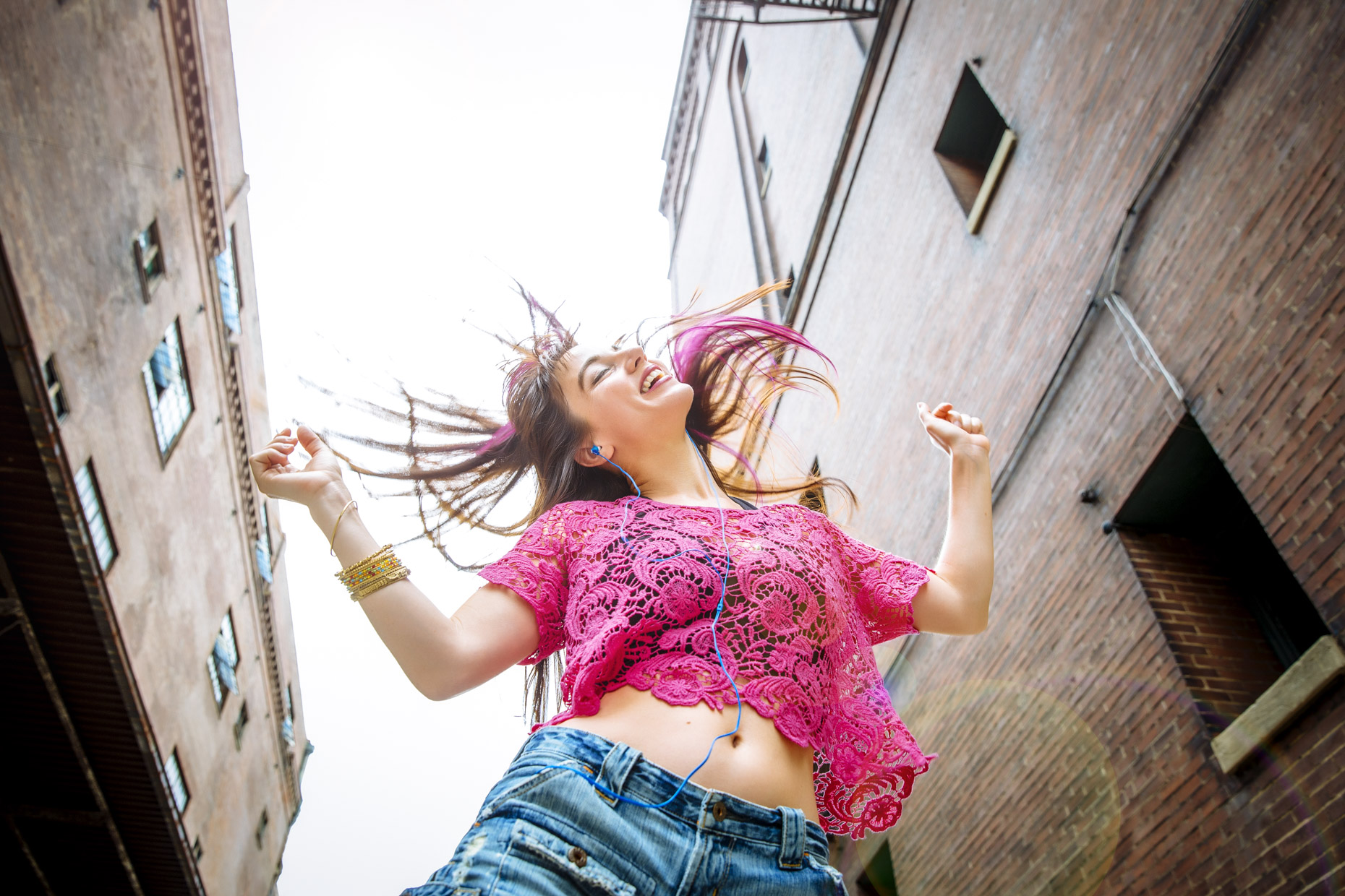 Happy woman with pink hair, lace shirt and blue headphones dancing in the street