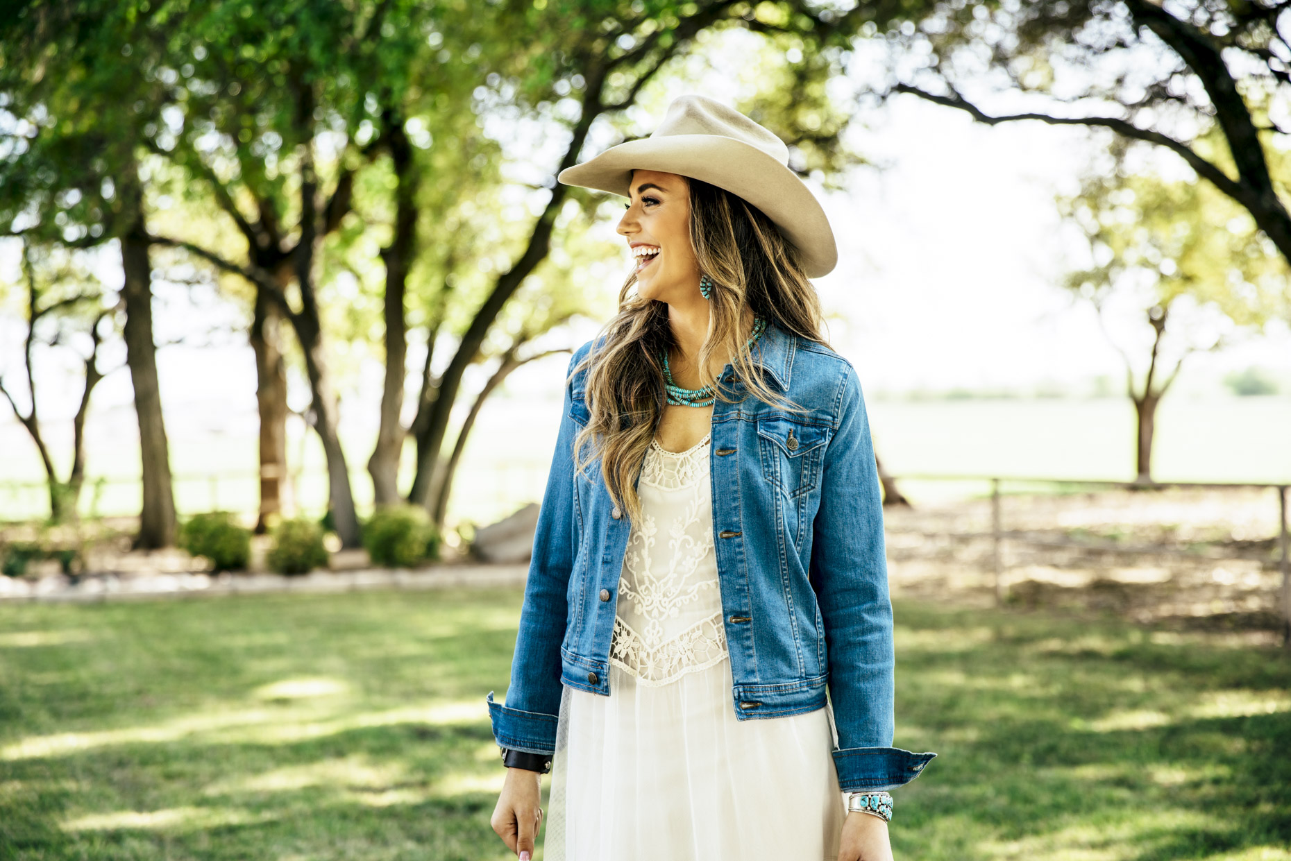 Happy woman in white dress denim wrangler jacket and cowboy hat outside