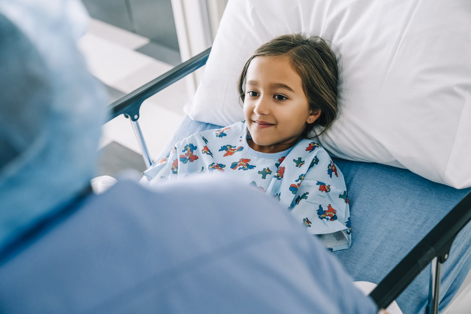 Hispanic girl in hospital bed smiling nervously at nurse