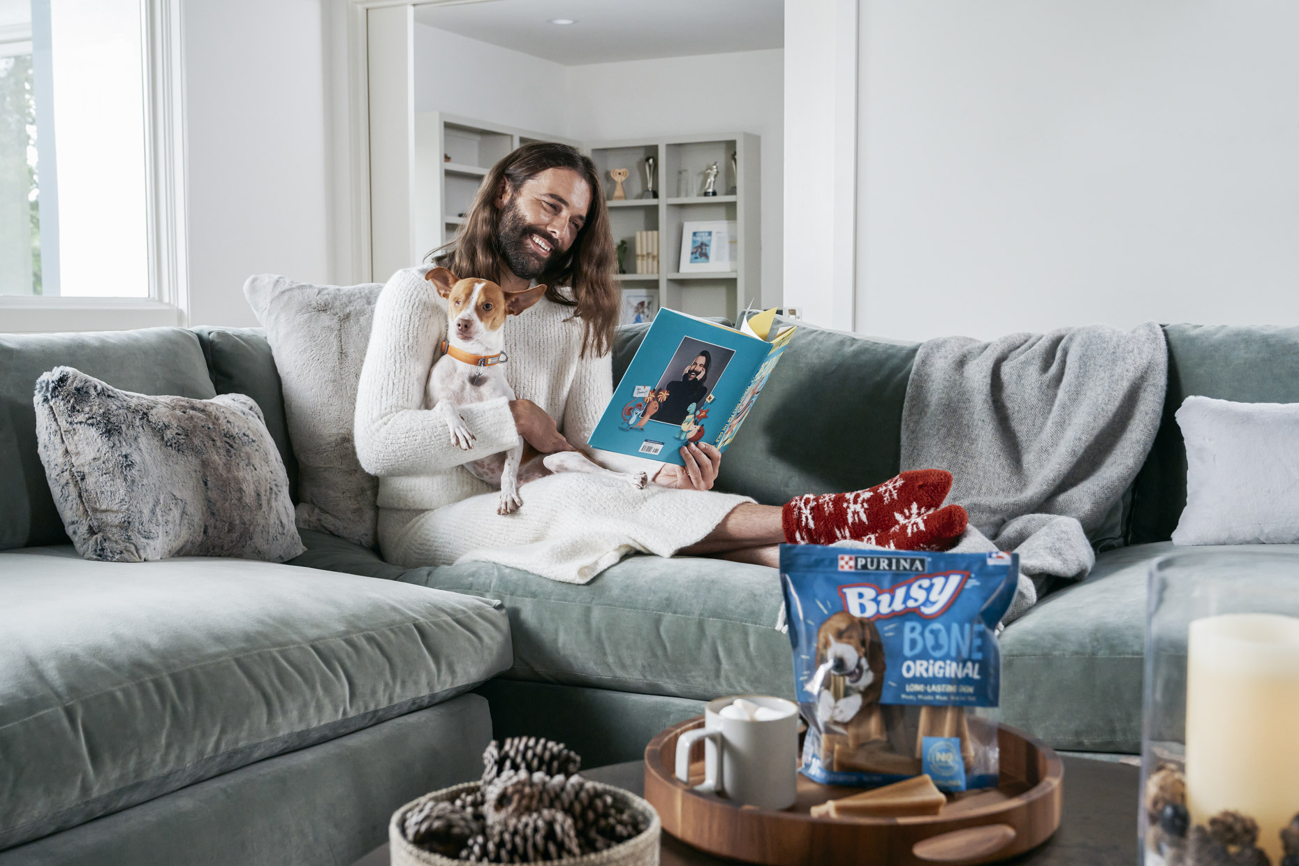 Jonathan Van Ness pet dog Pablo on couch with Purina Busy Bone treat reading book