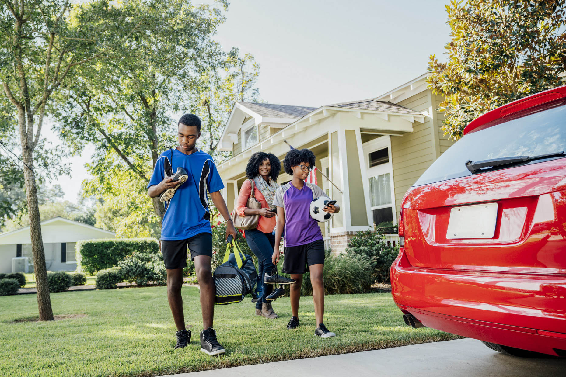 Kids in sports attire walking toward car with mom