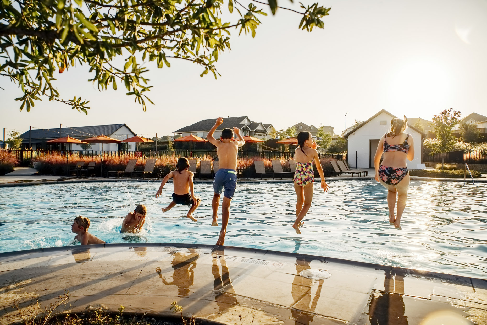 Kids jumping into pool in summer sunlight