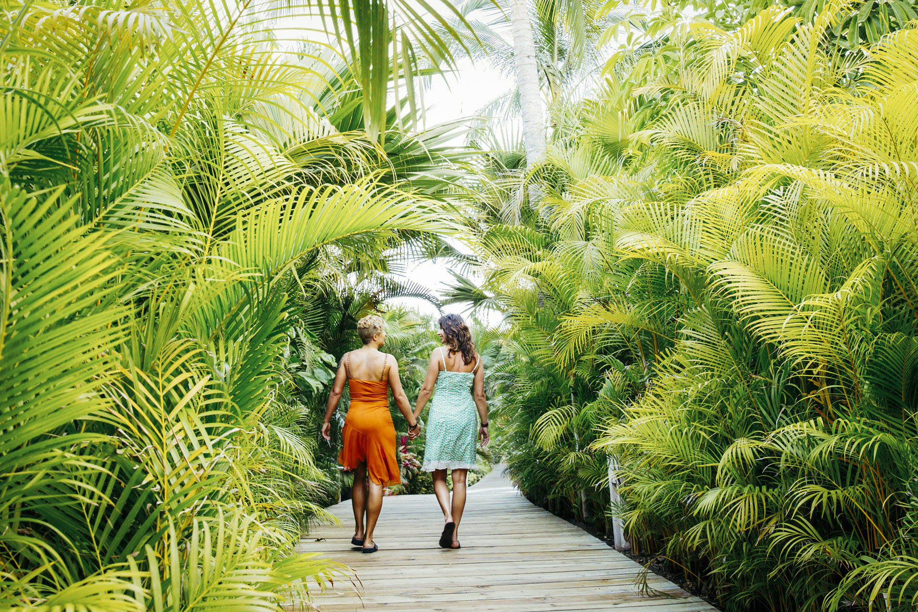 Lesbian couple walking holding hands on path in tropical Mexico