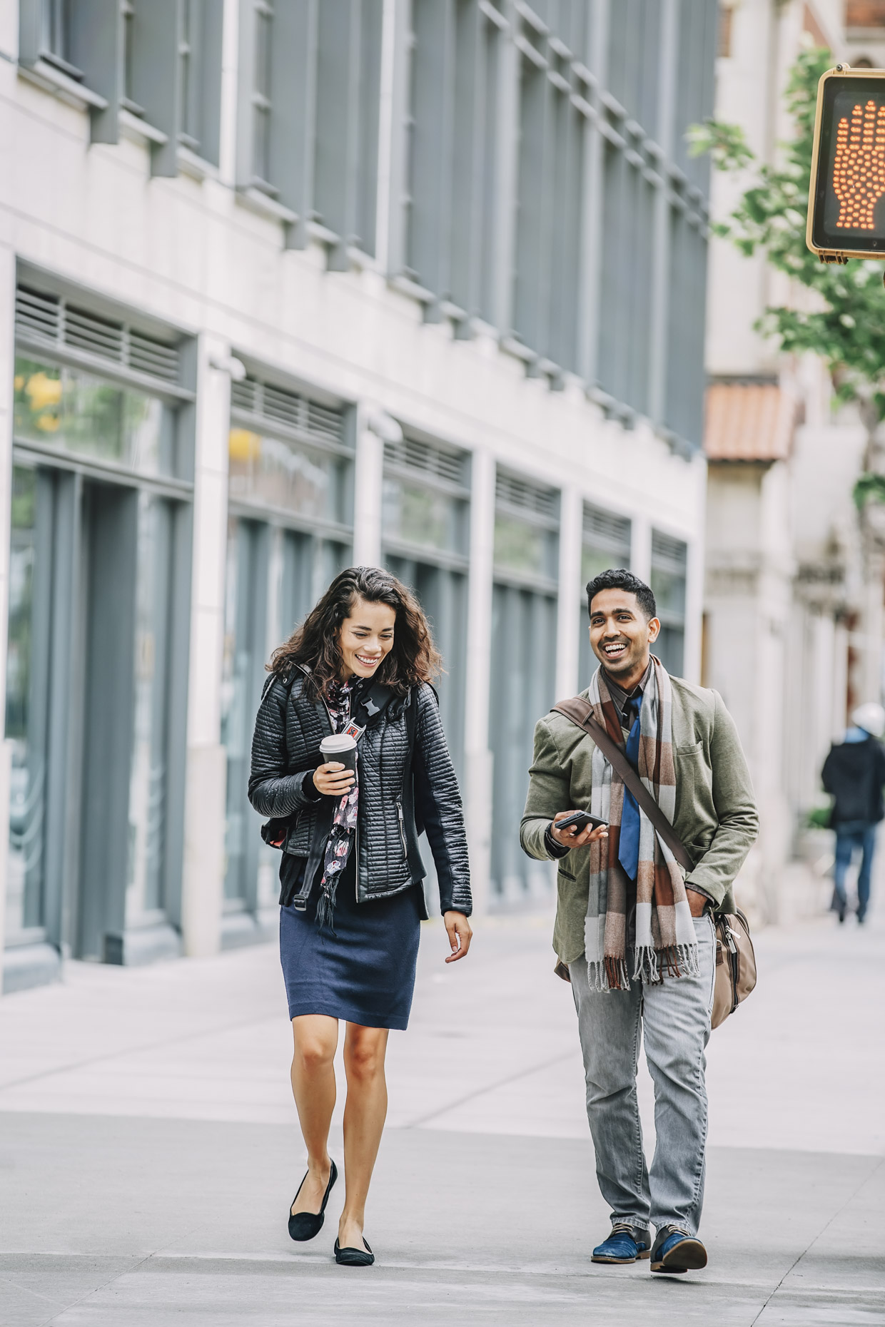 Man and woman walking down sidewalk in fall clothes drinking coffee and laughing