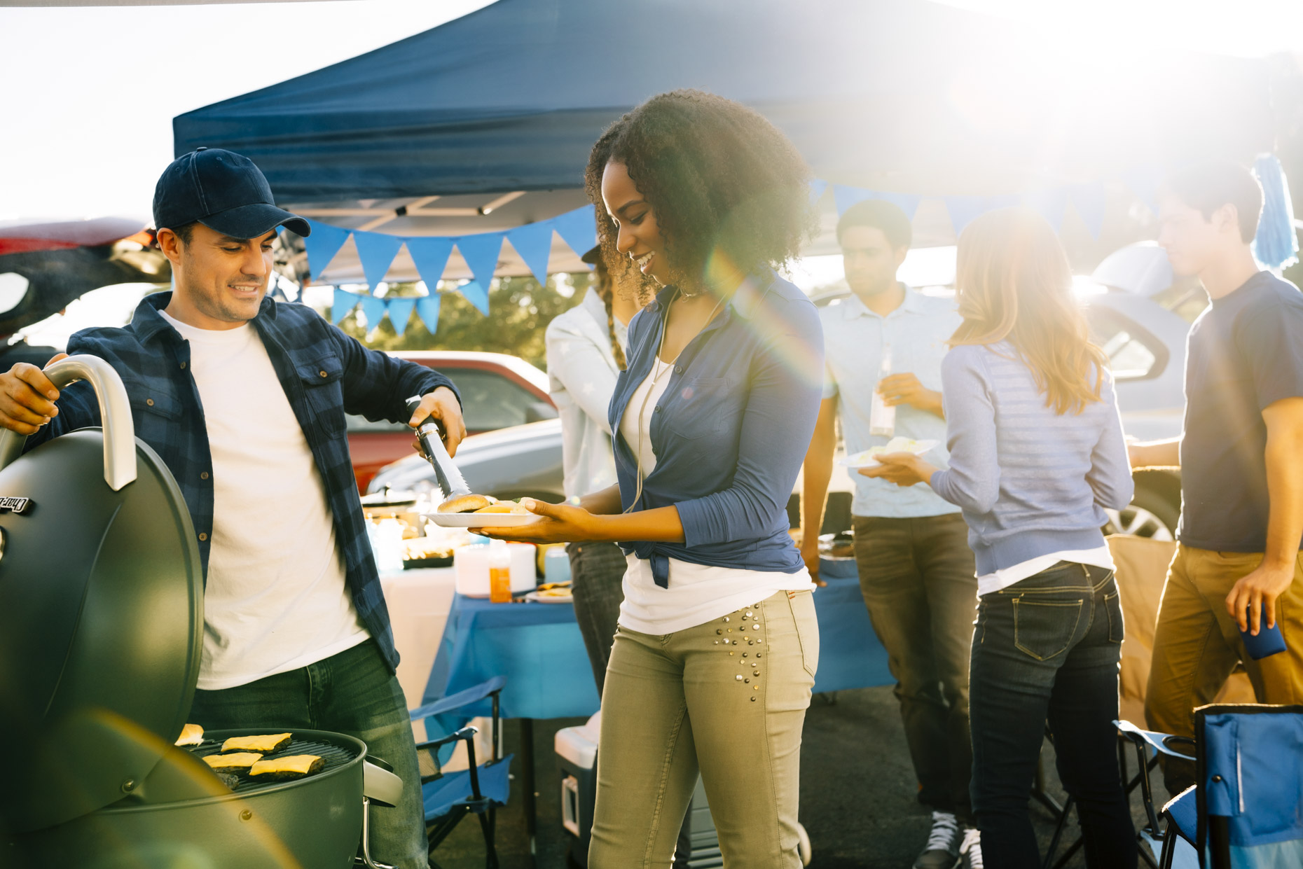 Man giving woman hamburger from grill at tailgate party