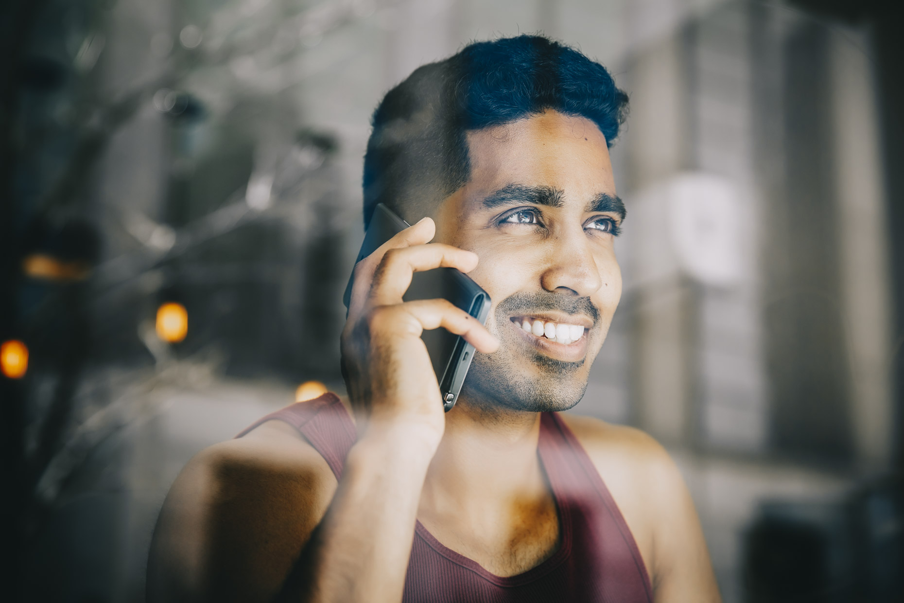 Man in maroon tank top talking on cell phone looking out window