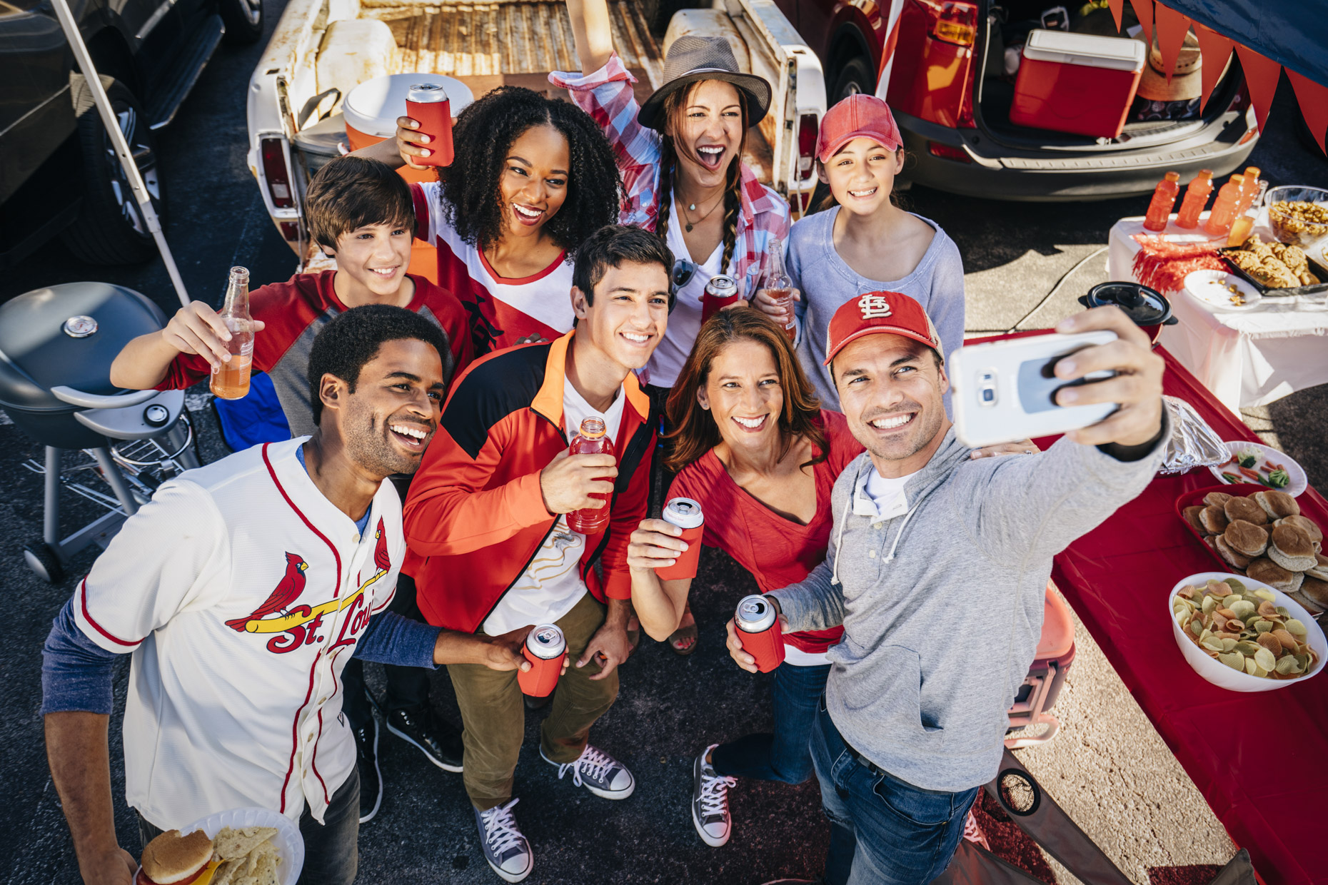 Man taking selfie photo with phone of tailgating group of sports fans