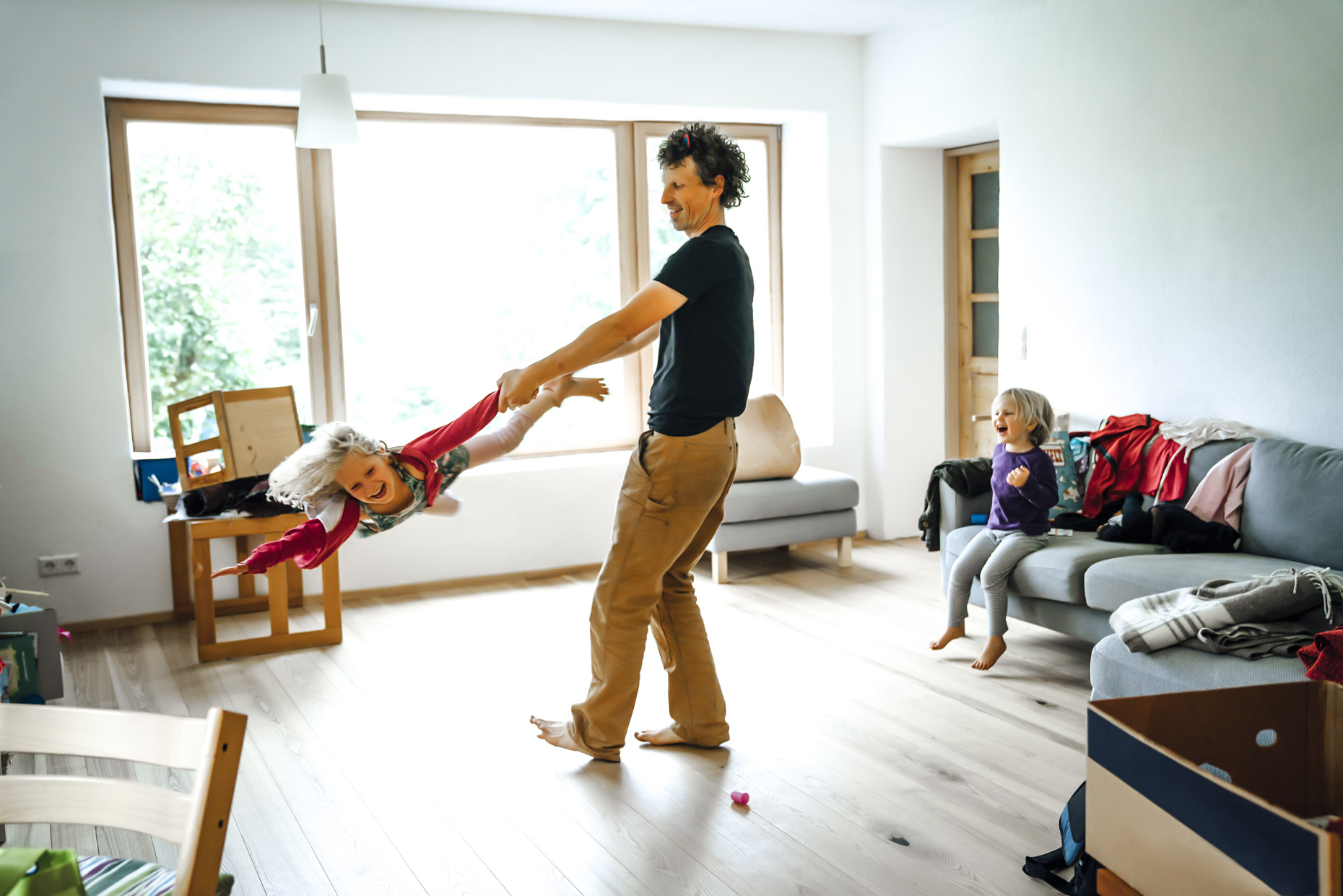 Man twirling happy daughter around messy living room