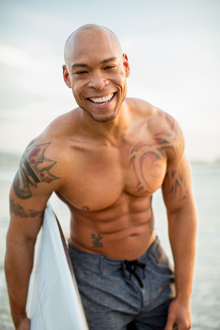 Man-with-surf-board-at-beach-smiling-tattoos-is201303247647